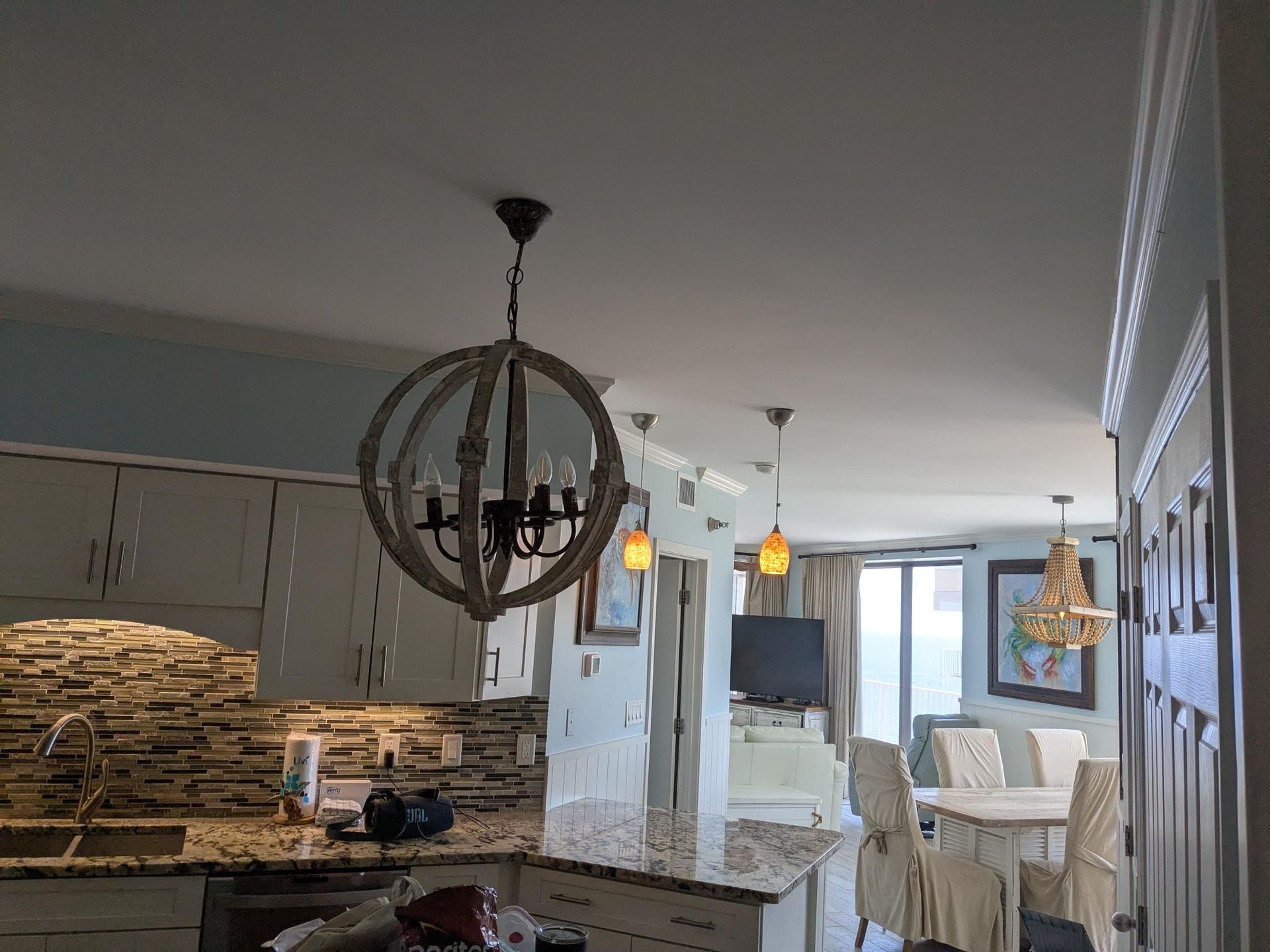 Kitchen with globe chandelier, stone backsplash, and dining area with chandelier and table.