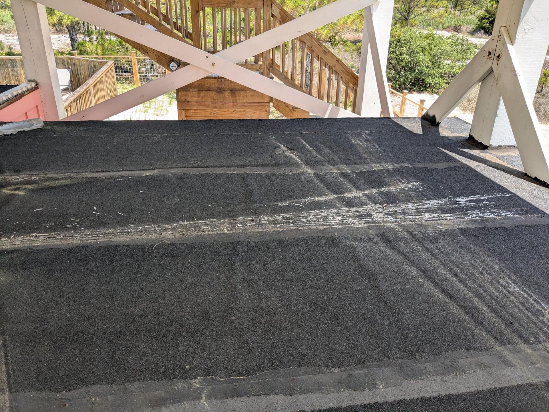 Dark textured platform with white railing, partially covering wooden stairs; sunlight.