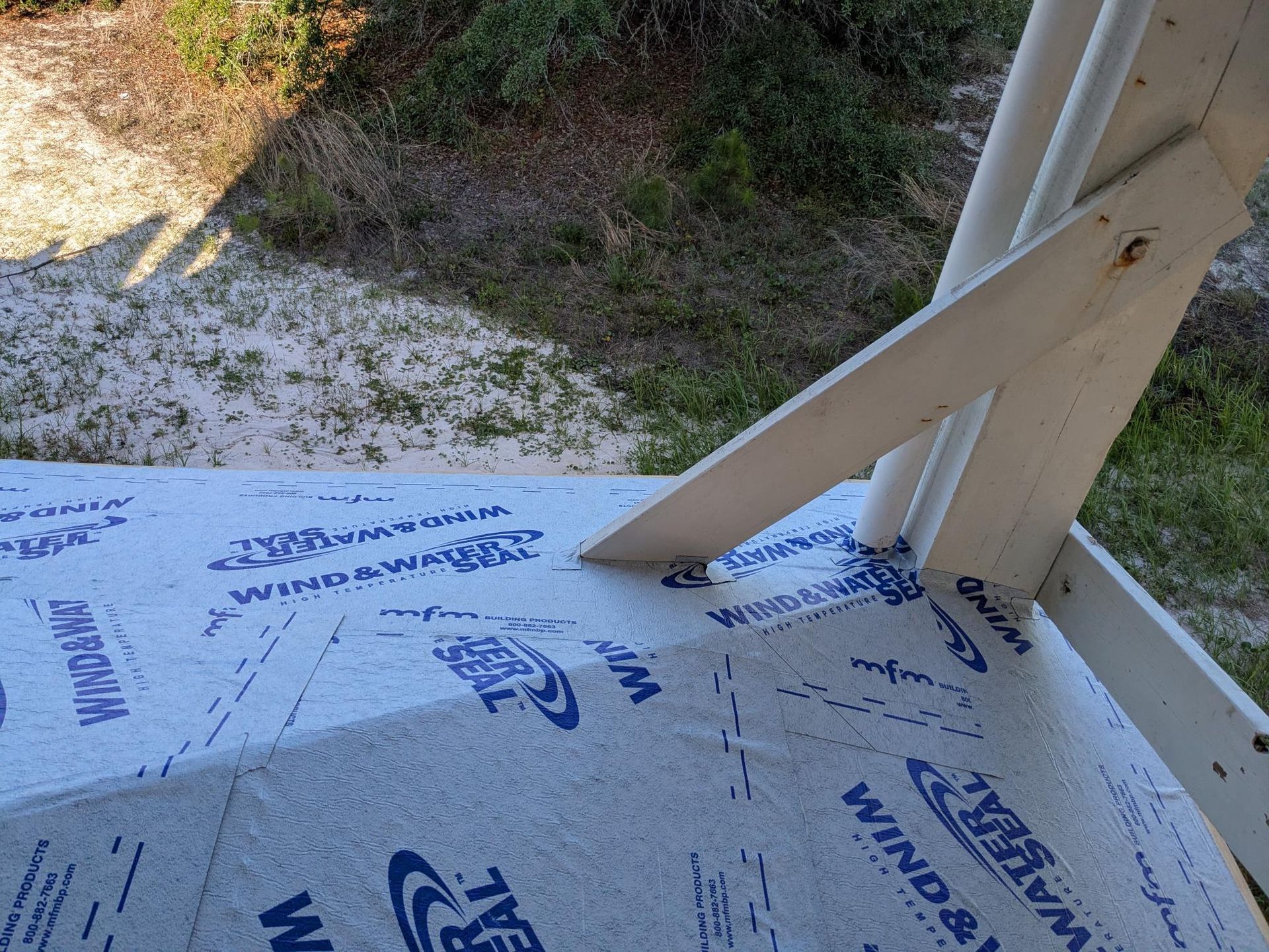 Close-up of a roof under construction, showing blue waterproof membrane and wooden support beams in an outdoor setting.