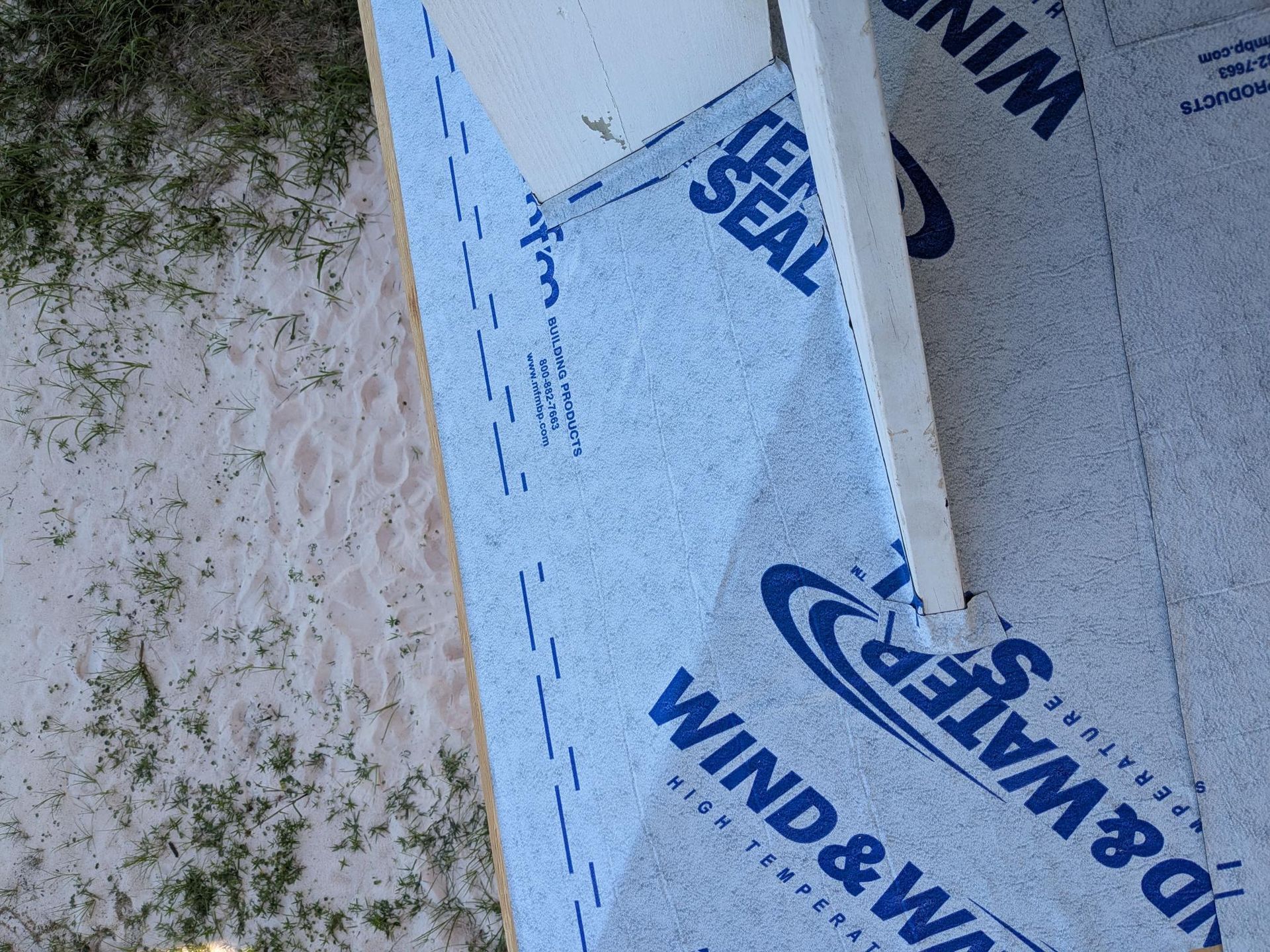Blue Wind & Water barrier material installed on a building's corner, with white framing visible.