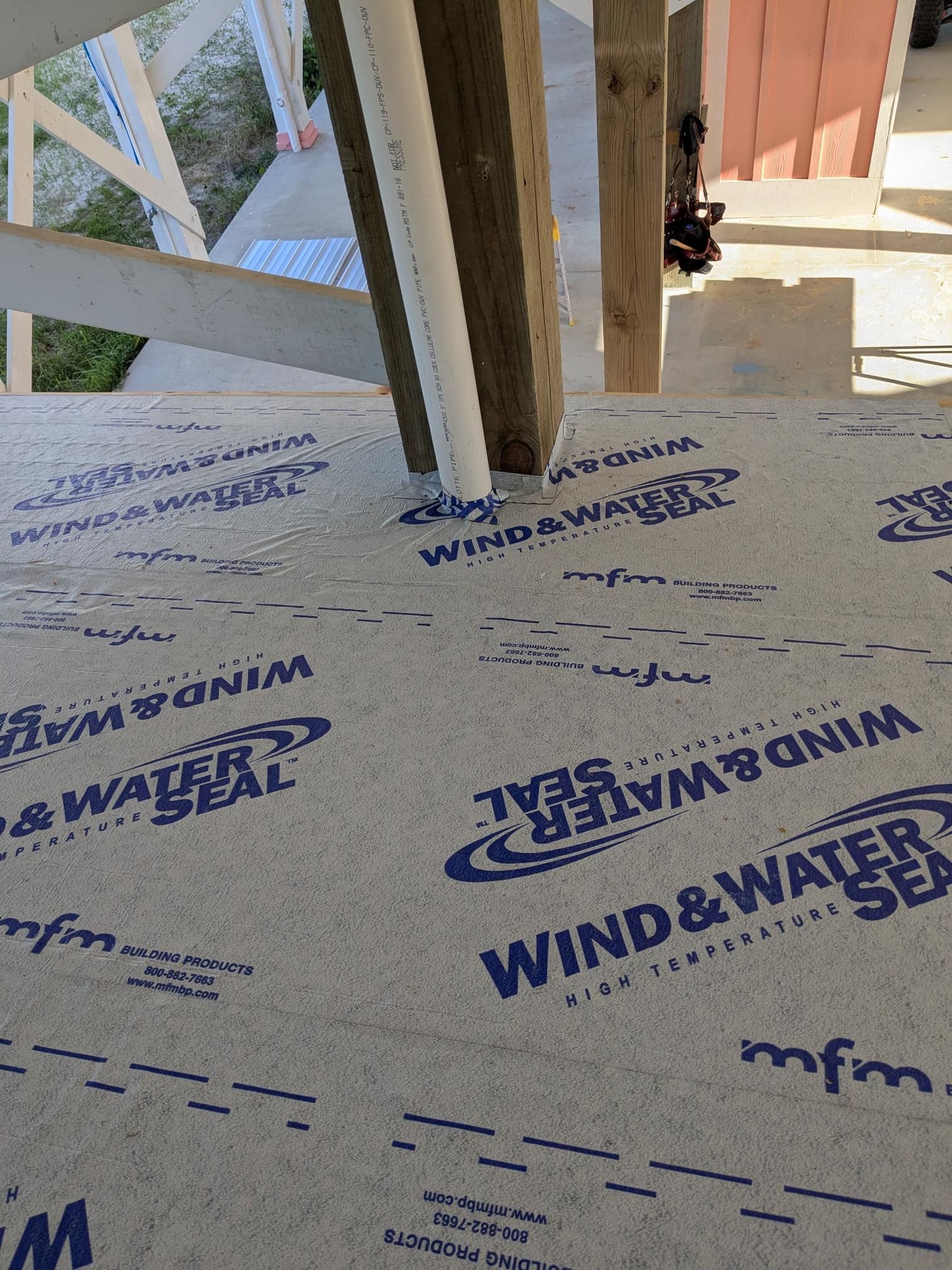 Close-up of Wind & Water Seal material covering a wooden structure. Blue text on gray surface.