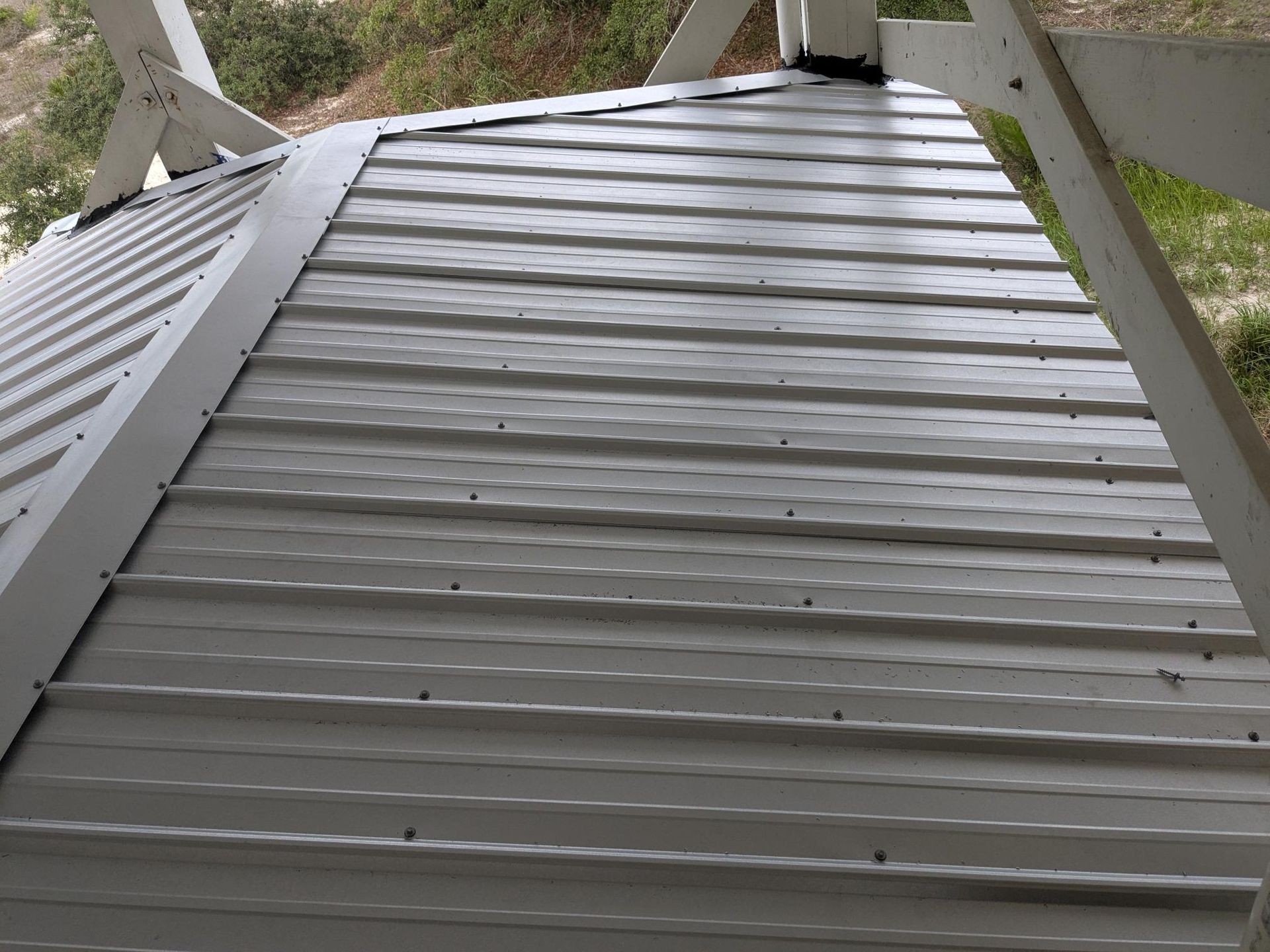 Gray metal roof with horizontal ribbed panels, attached to a white wooden structure.