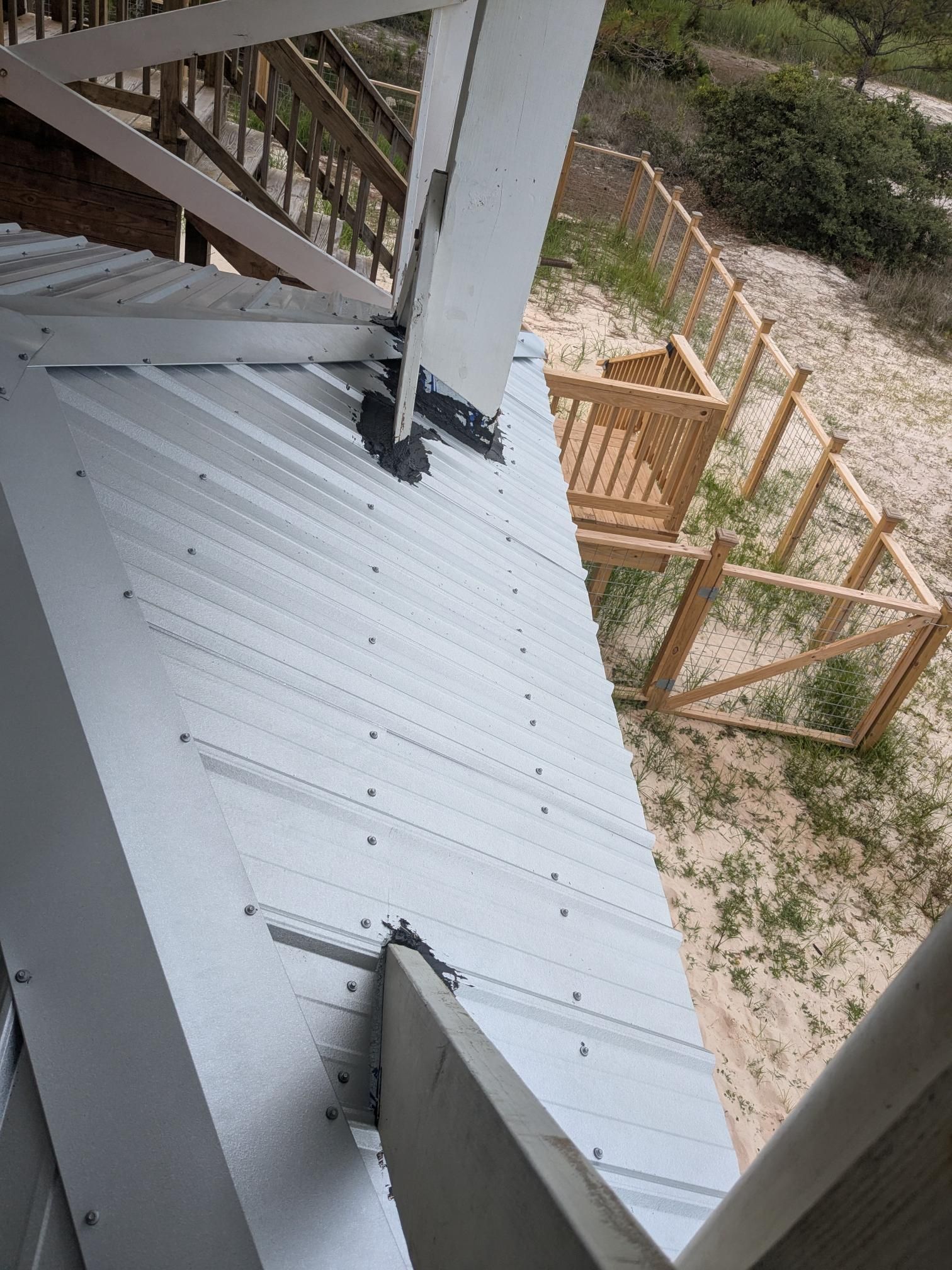 Metal roof with wooden beams, stairs, and a small fenced area.