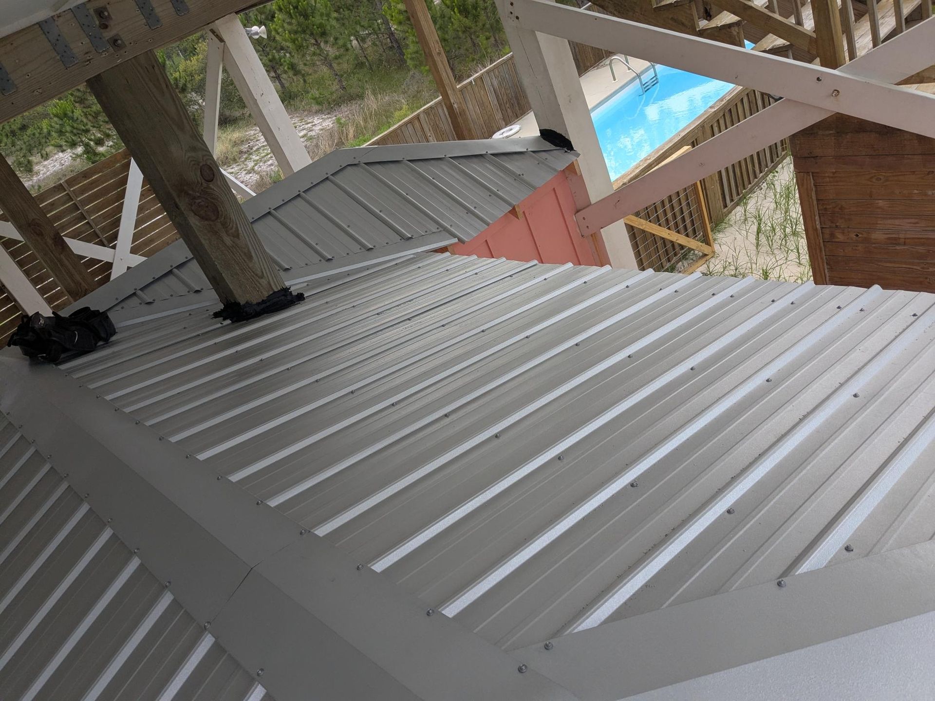Metal roof of gazebo with white support beams; pool visible in background.