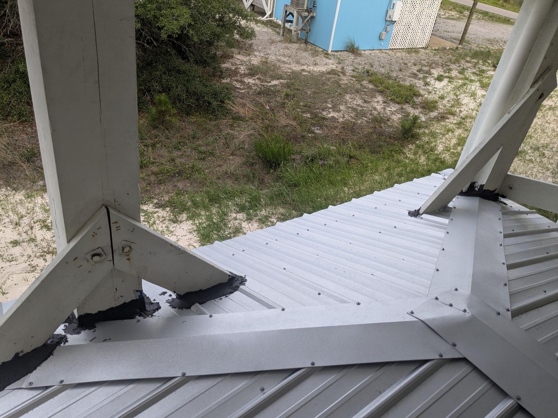 View from a white gazebo roof, showing white supports and corrugated metal panels; grass and a blue building in background.