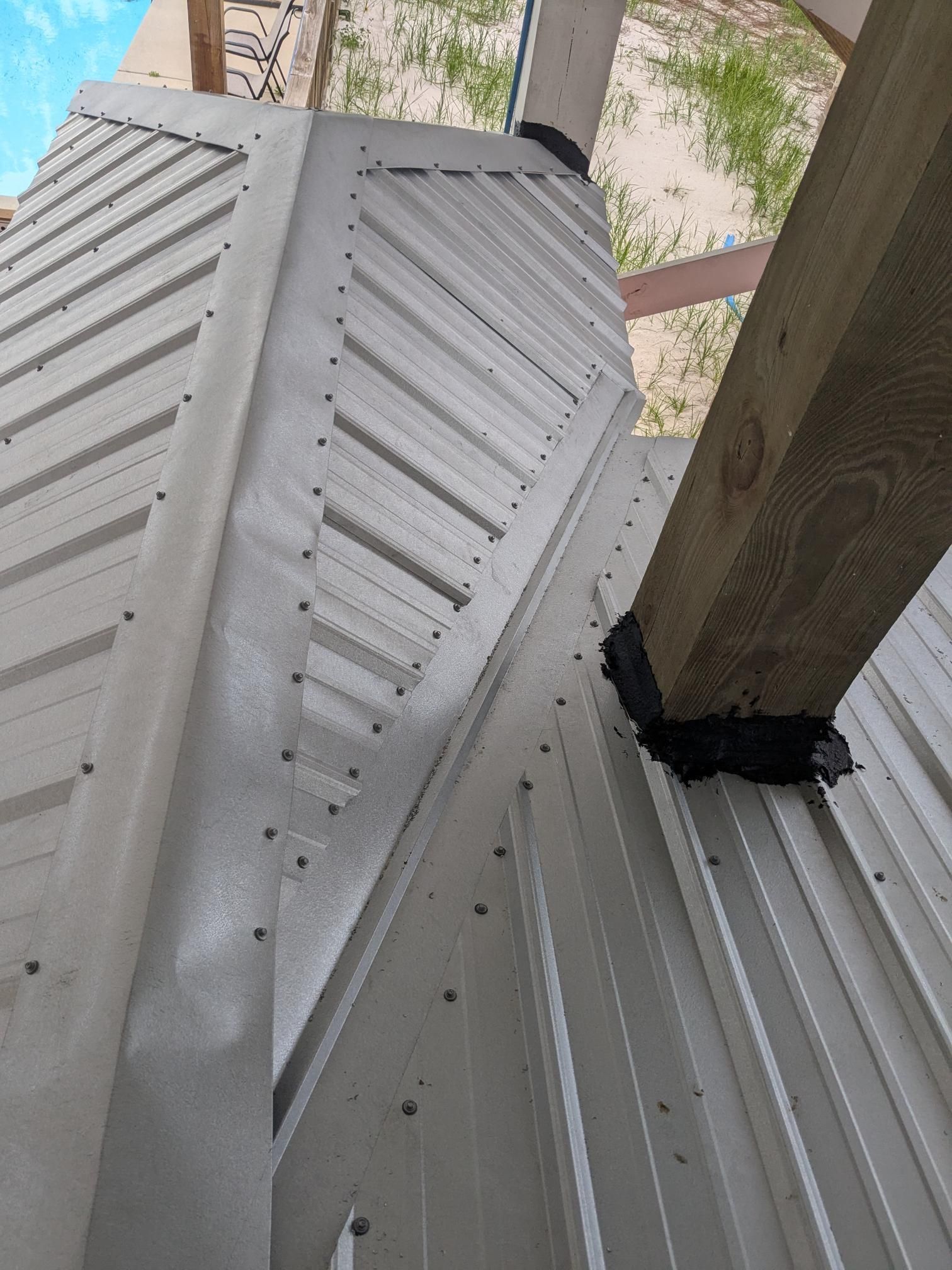 Metal siding with diagonal lines, supporting a wooden beam. Fasteners are visible.