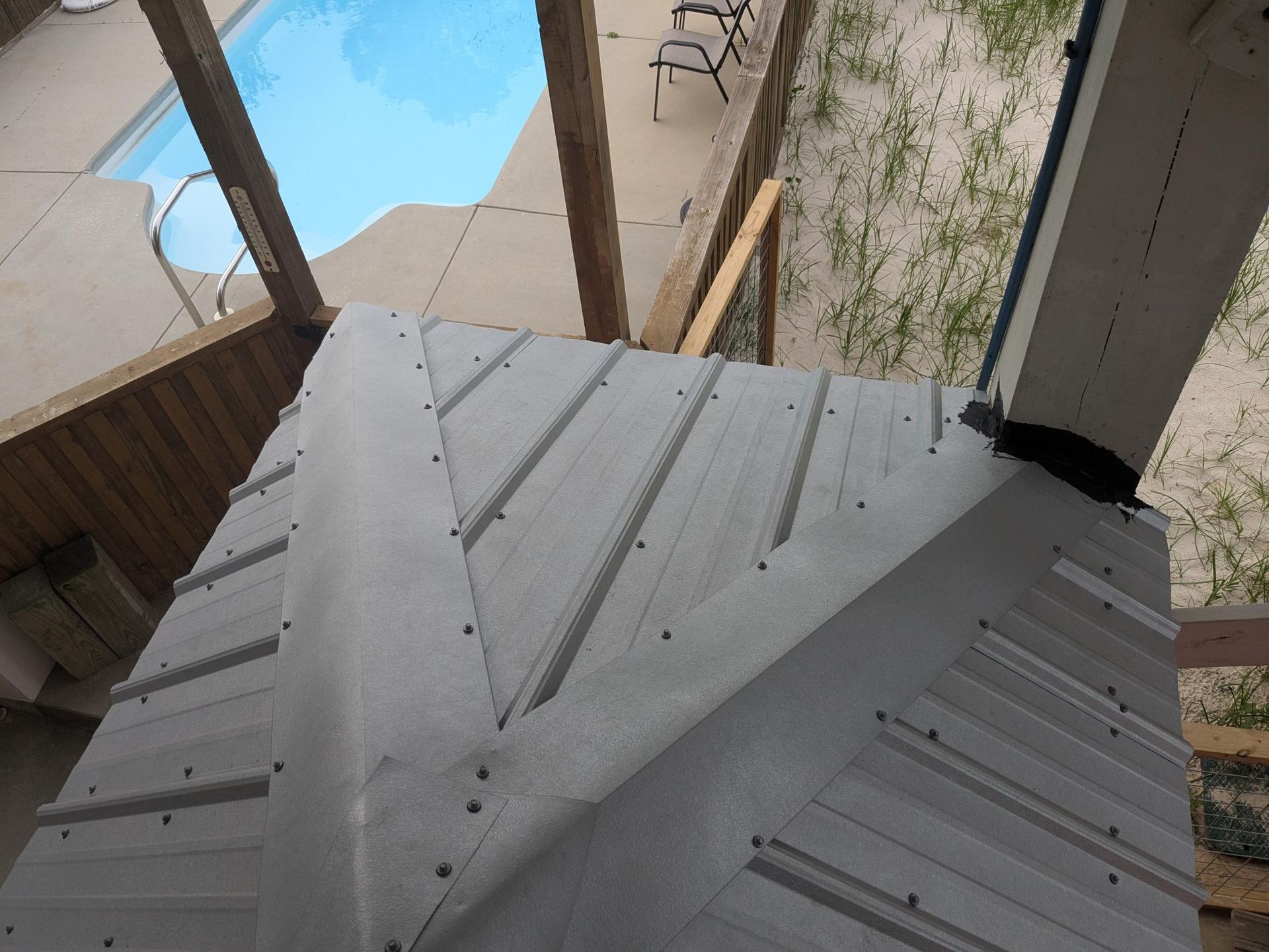 Gray angular roof structure with visible screw heads, possibly under construction near a pool.