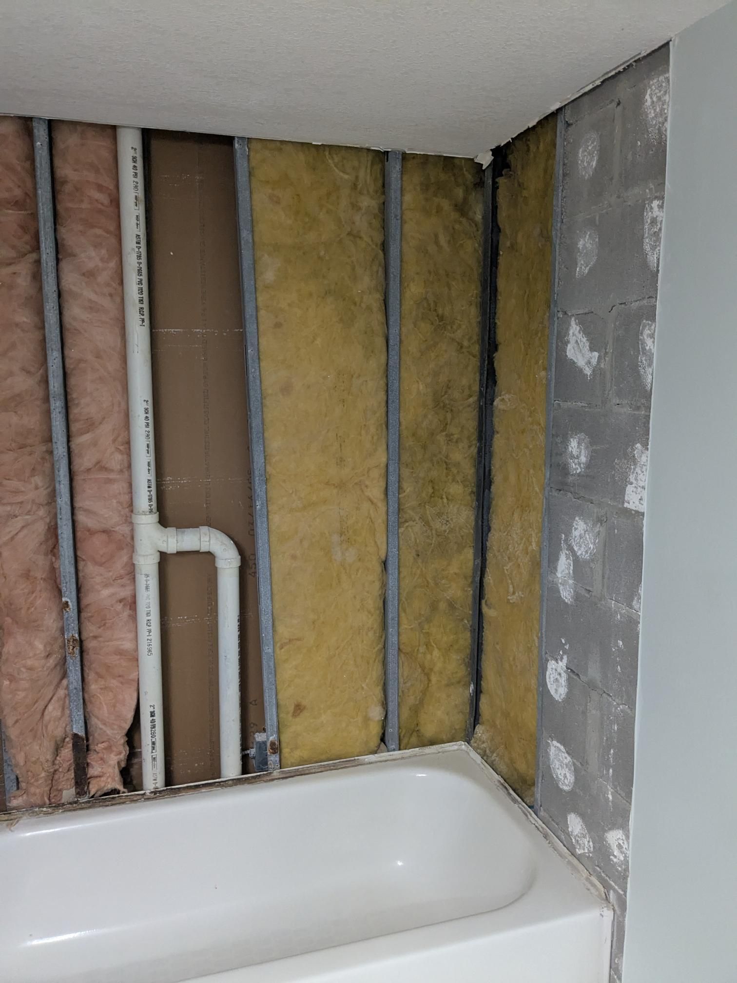 Bathroom wall under construction, insulation exposed, next to a white bathtub.