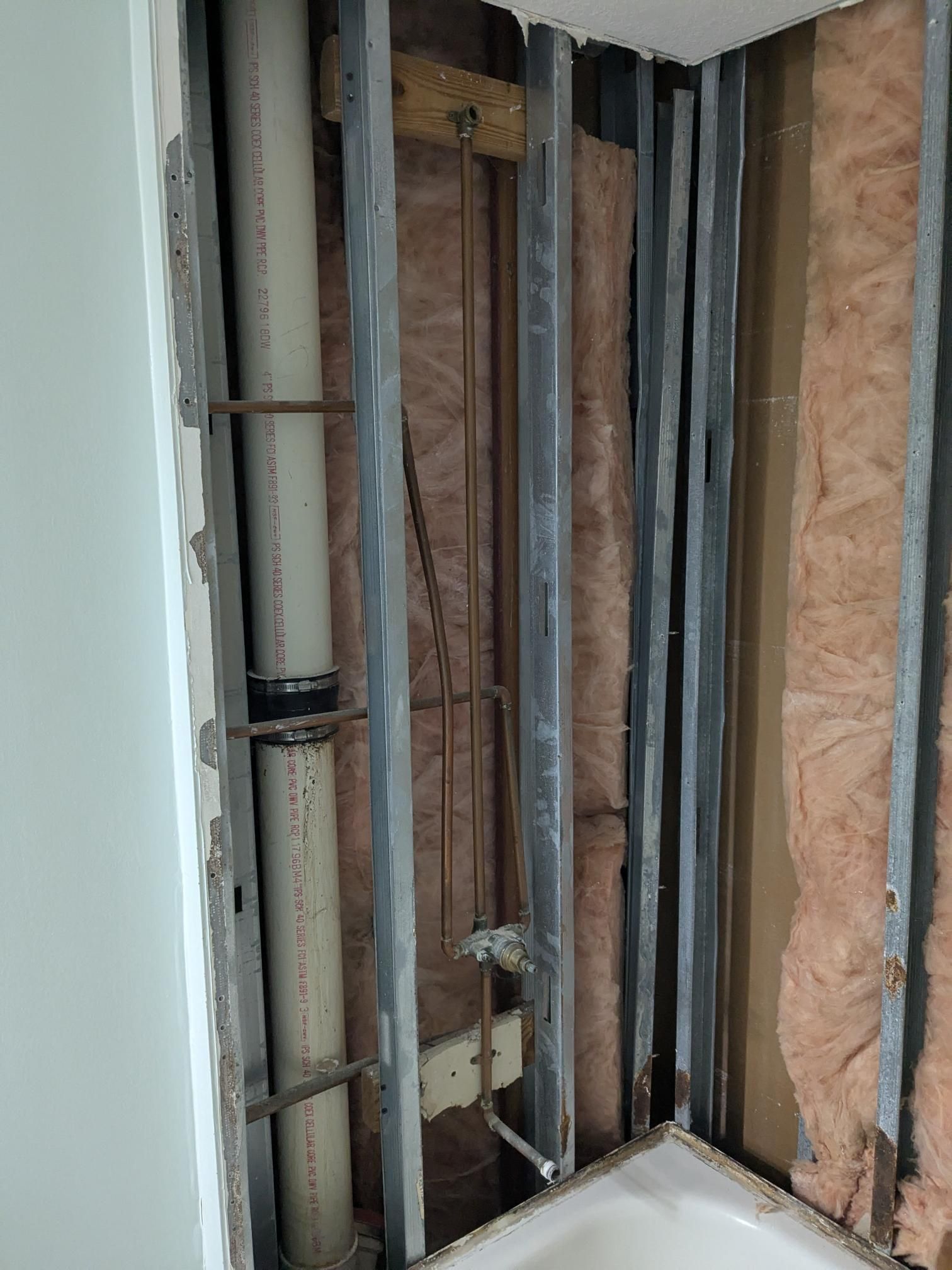 Exposed plumbing in a bathroom wall. White PVC pipes are visible, as well as copper pipes and insulation.