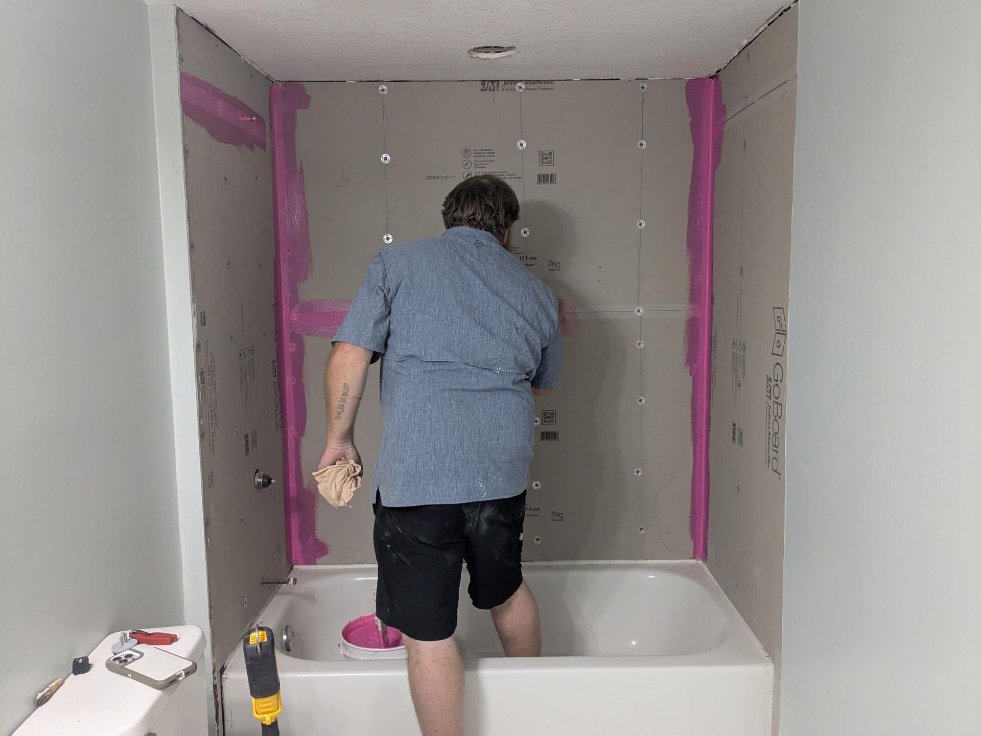 Person inside a bathtub, working on the shower walls, which are gray. Pink sealant is visible.