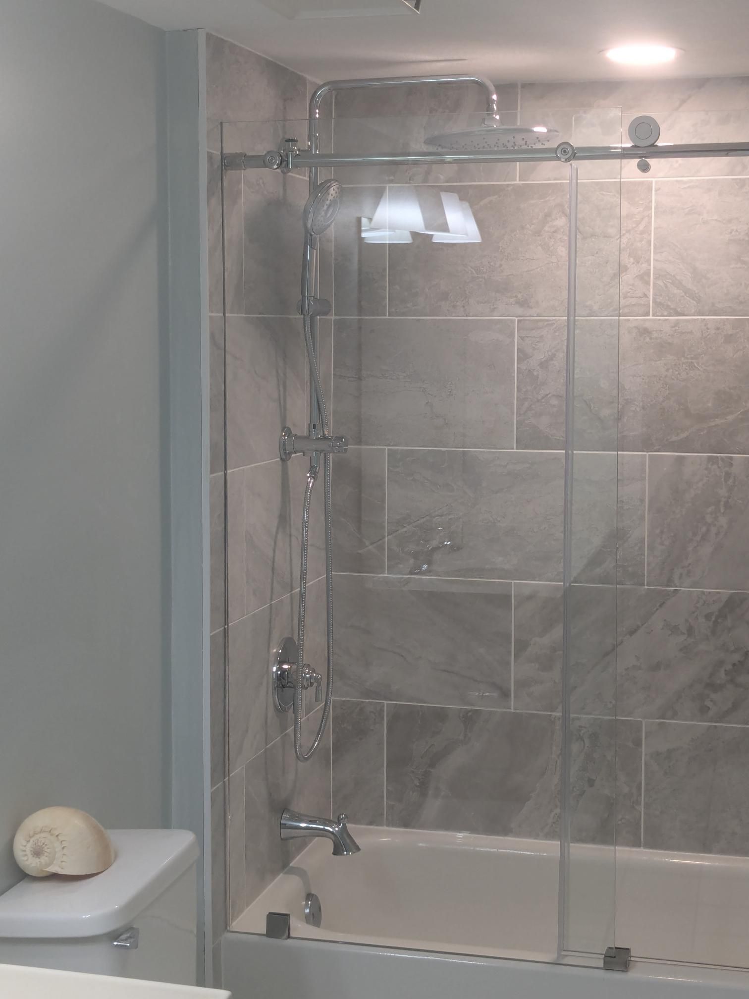Bathroom with gray tiled walls, showerhead, and bathtub. A toilet and shell are also visible.