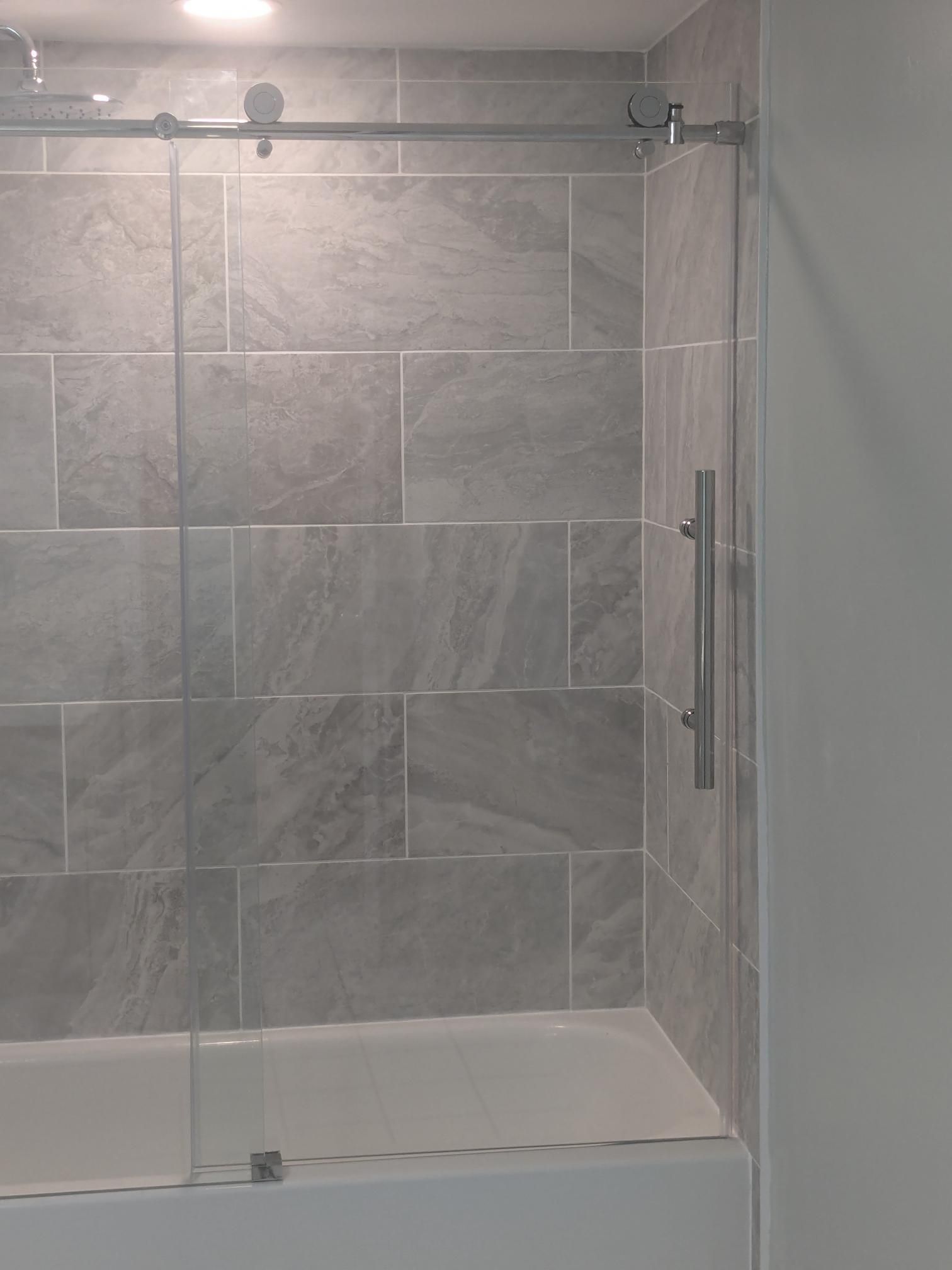 Shower with sliding glass door, grey tiled walls, and silver handle.