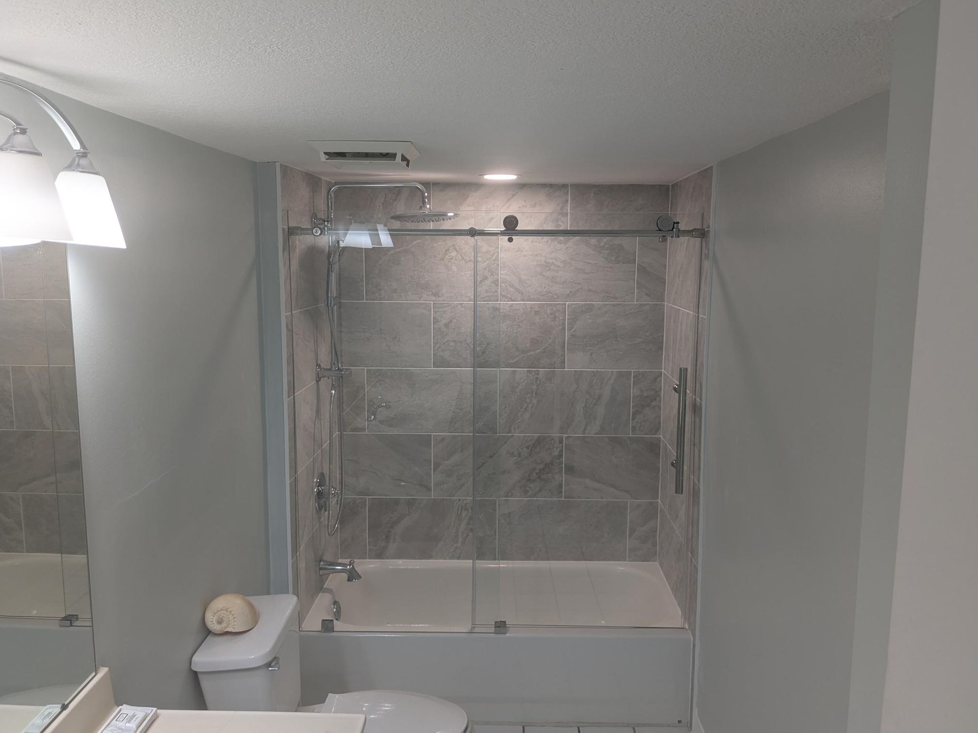 Bathroom with gray tile shower, glass door, and white tub and toilet.