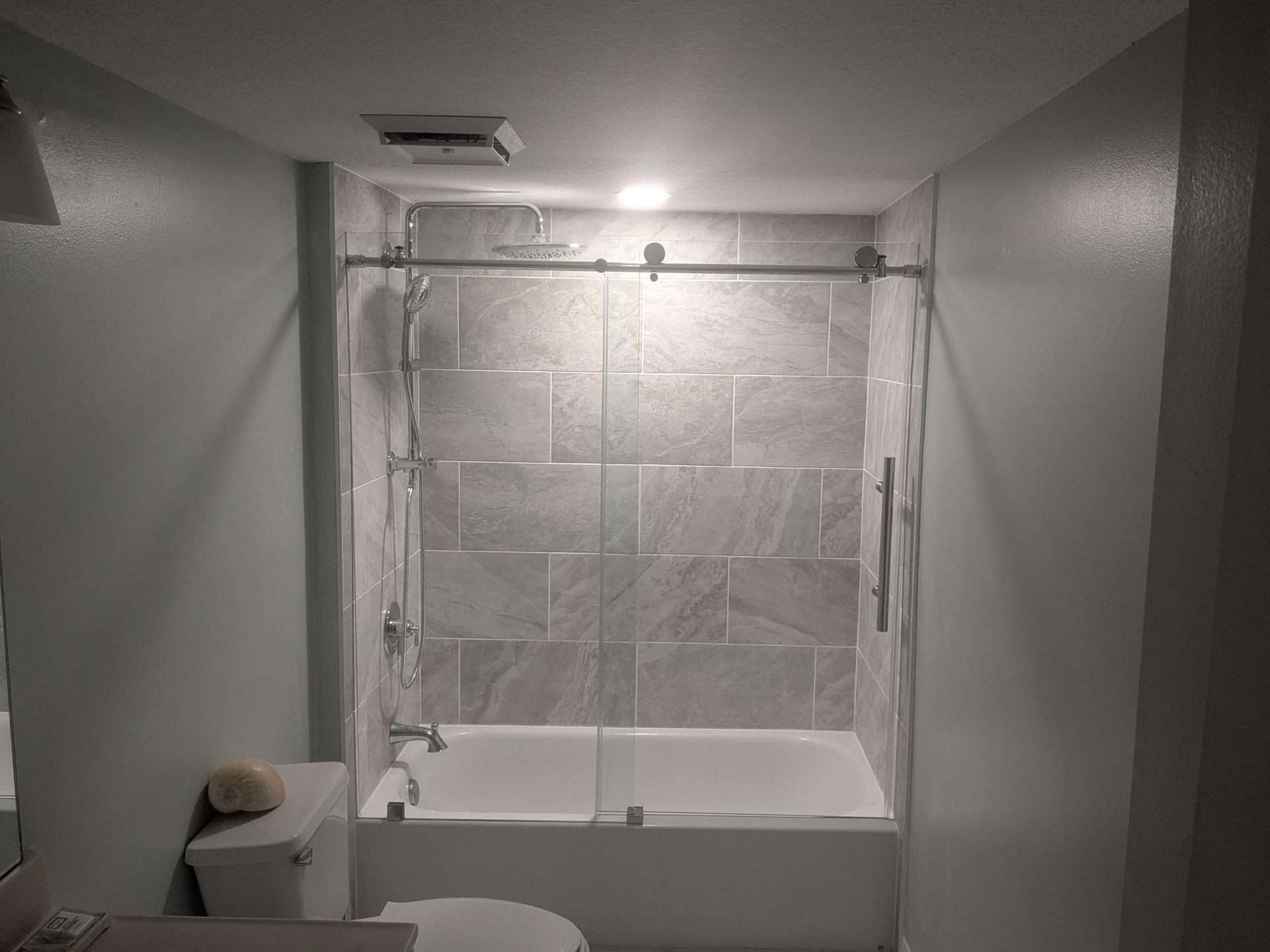 Bathroom with gray tiled shower, glass doors, and a white tub and toilet.
