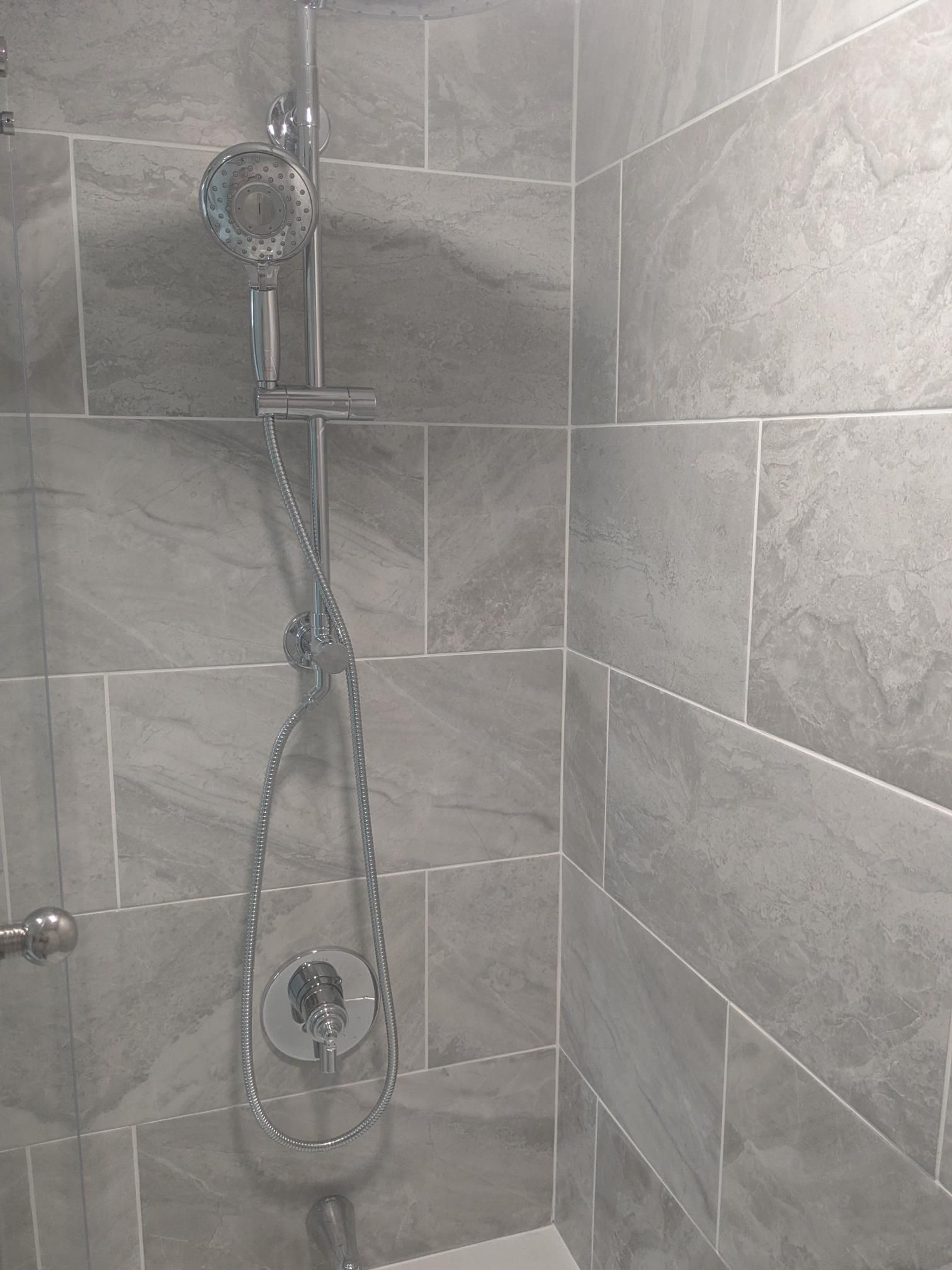 Gray tiled shower with handheld shower head and controls.