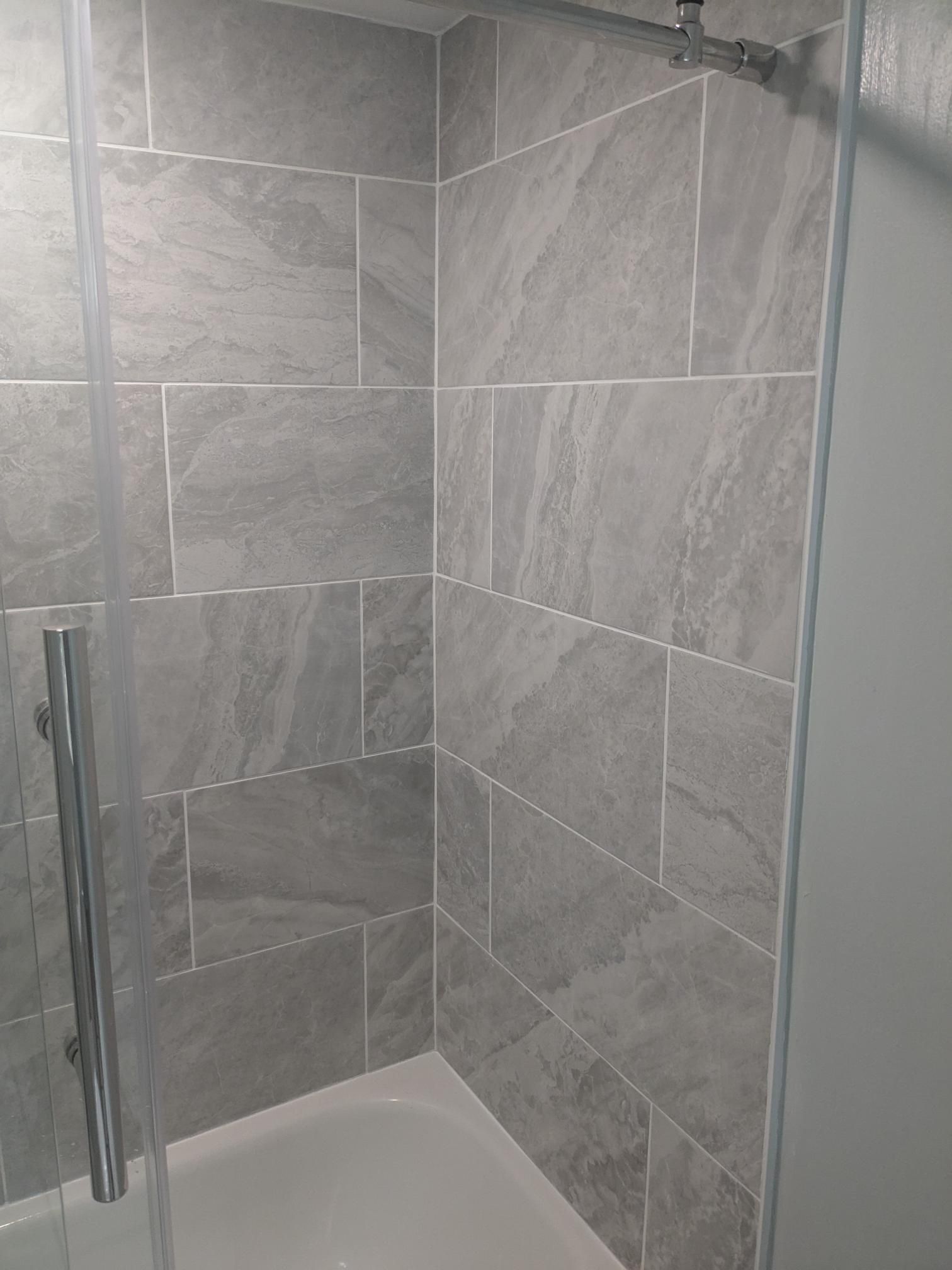 Grey tiled shower with glass door and silver handle.