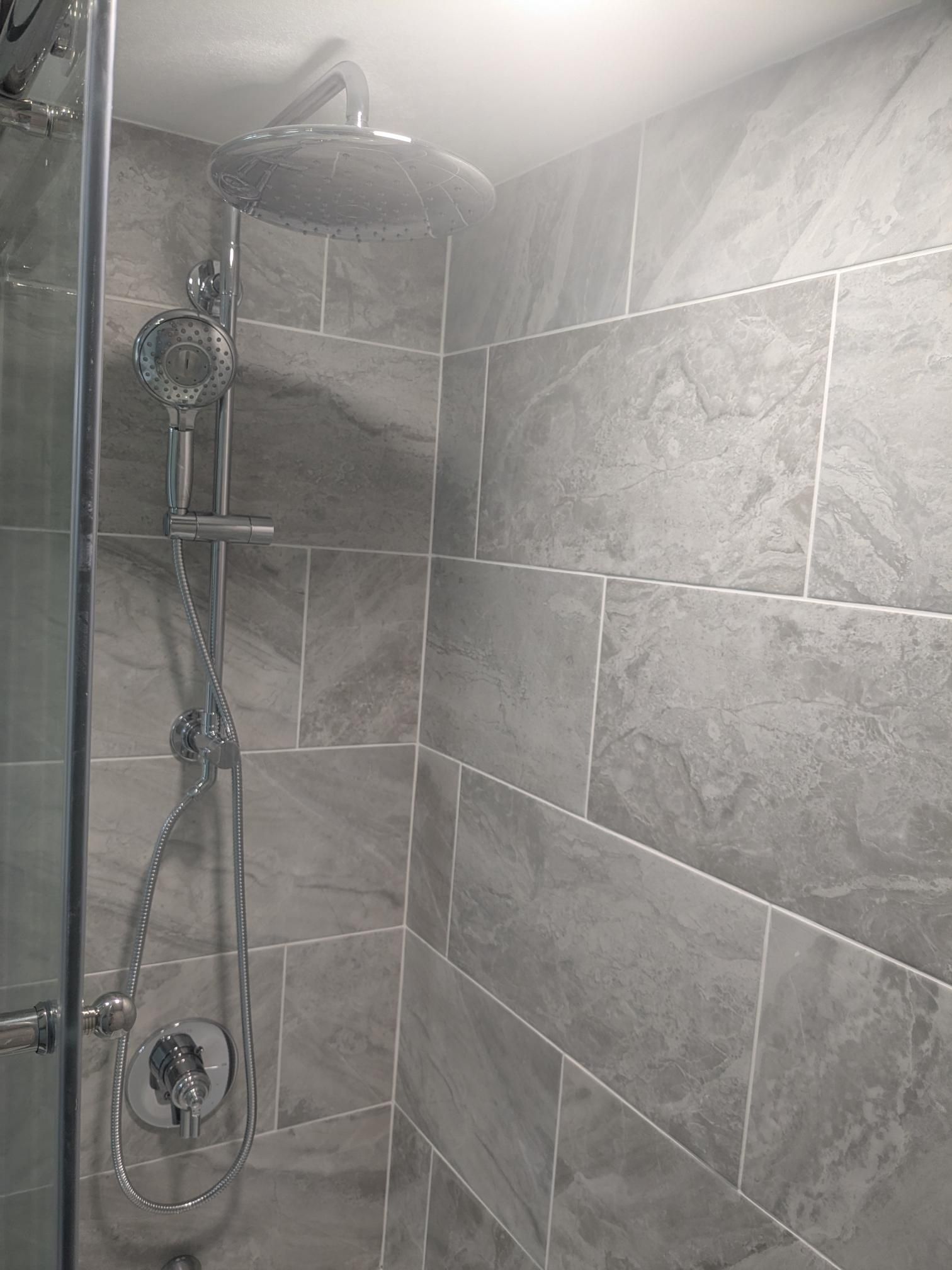 Shower stall with gray tile walls and chrome shower fixtures.