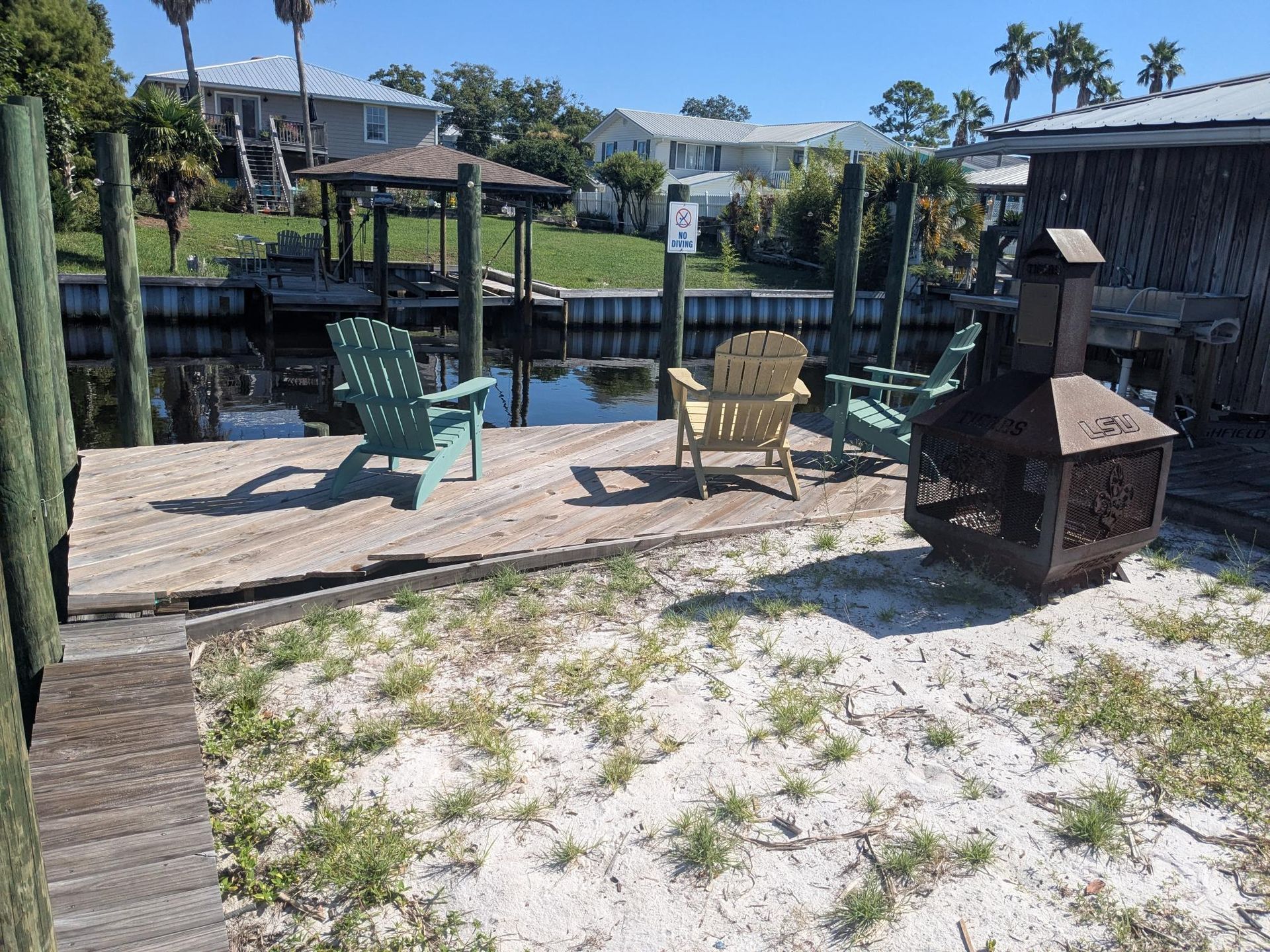 Dock with Adirondack chairs and a fire pit, overlooking a waterway.