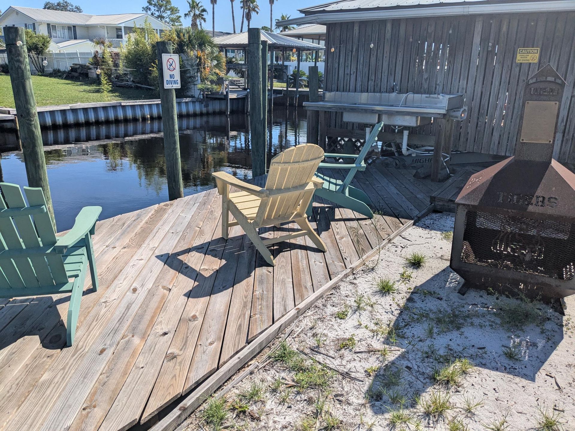 Dock with Adirondack chairs, fire pit, and small wooden shed next to a canal.