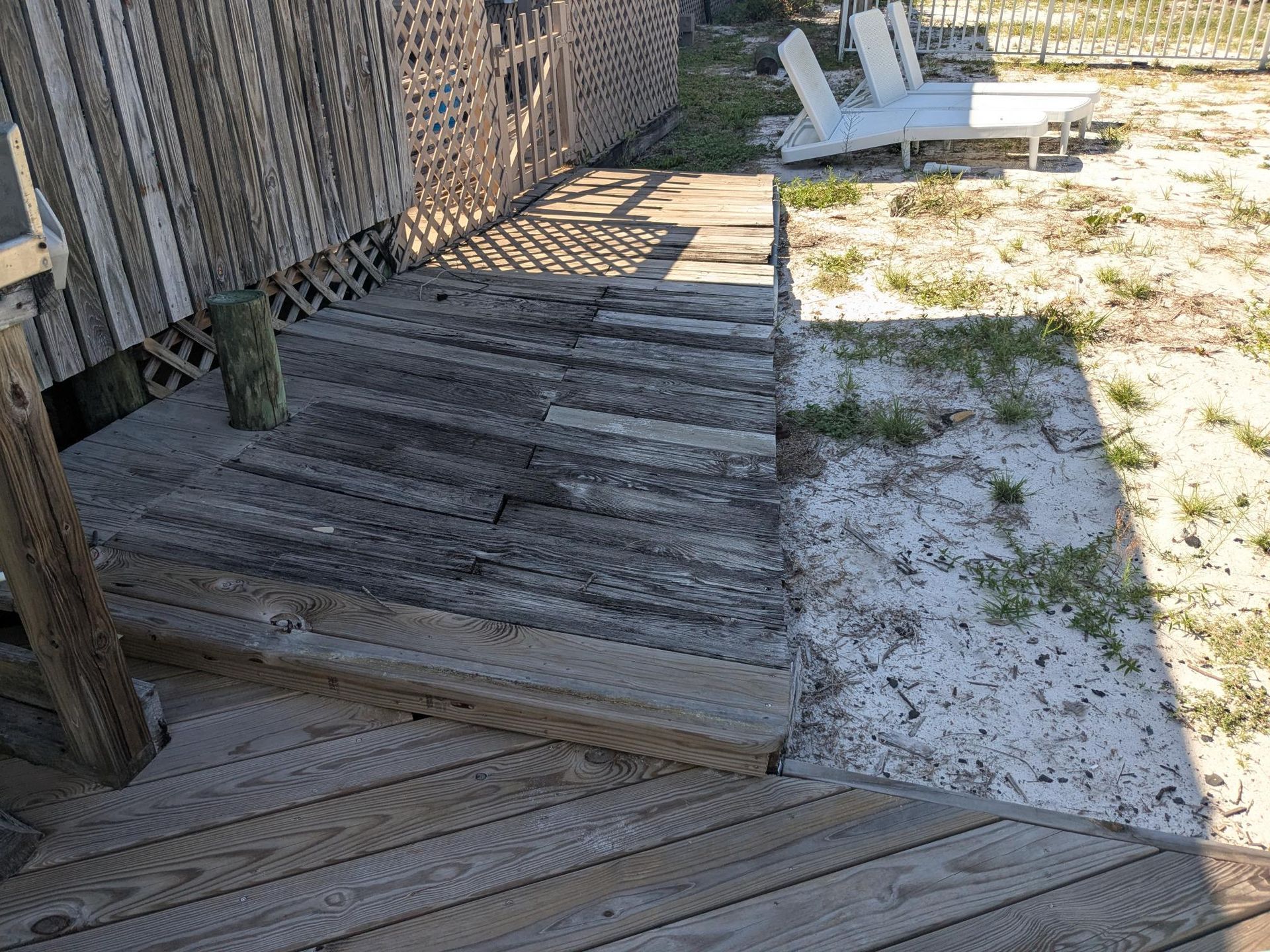 Wooden steps leading from a deck down to sandy ground near a building.