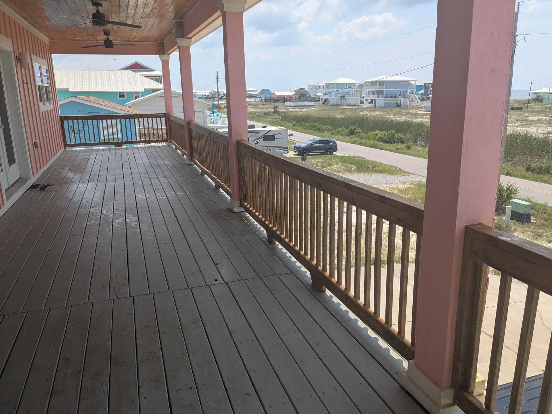 Covered porch with pink columns, wooden railing, overlooking a coastal neighborhood.