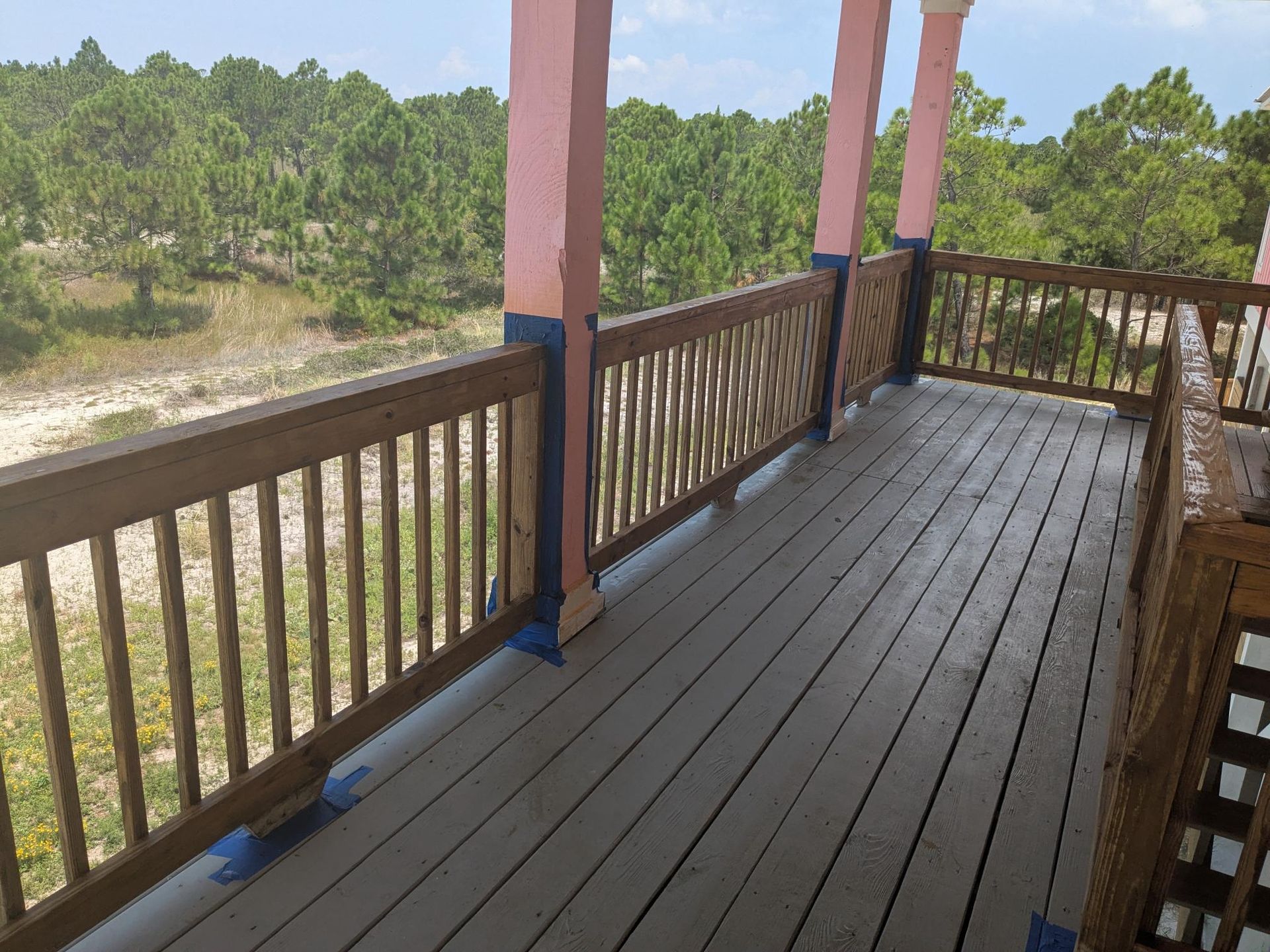 Wooden deck with railing overlooking a forest; pink columns support a roof.