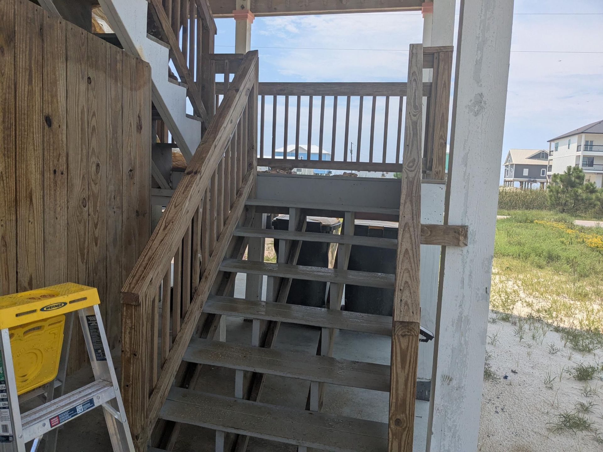 Wooden stairs leading up to a deck, near a beach. A yellow ladder rests below the stairs.