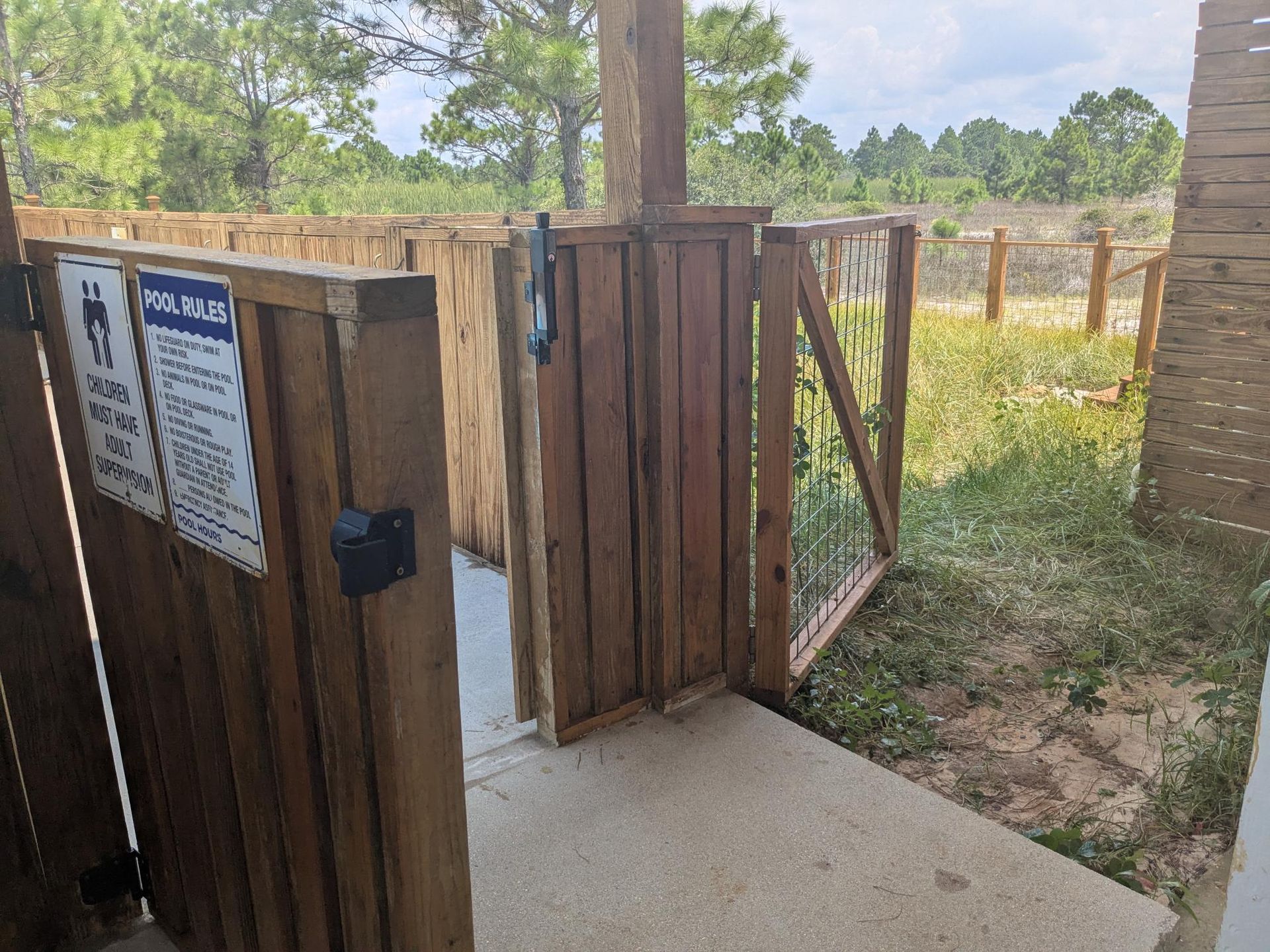 Wooden dog waste station with gated entrance, concrete path, and sign with instructions.