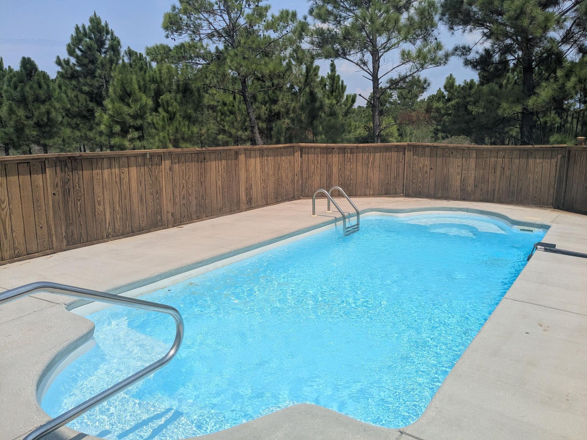 Rectangular in-ground pool surrounded by a wooden fence and concrete. Clear blue water.