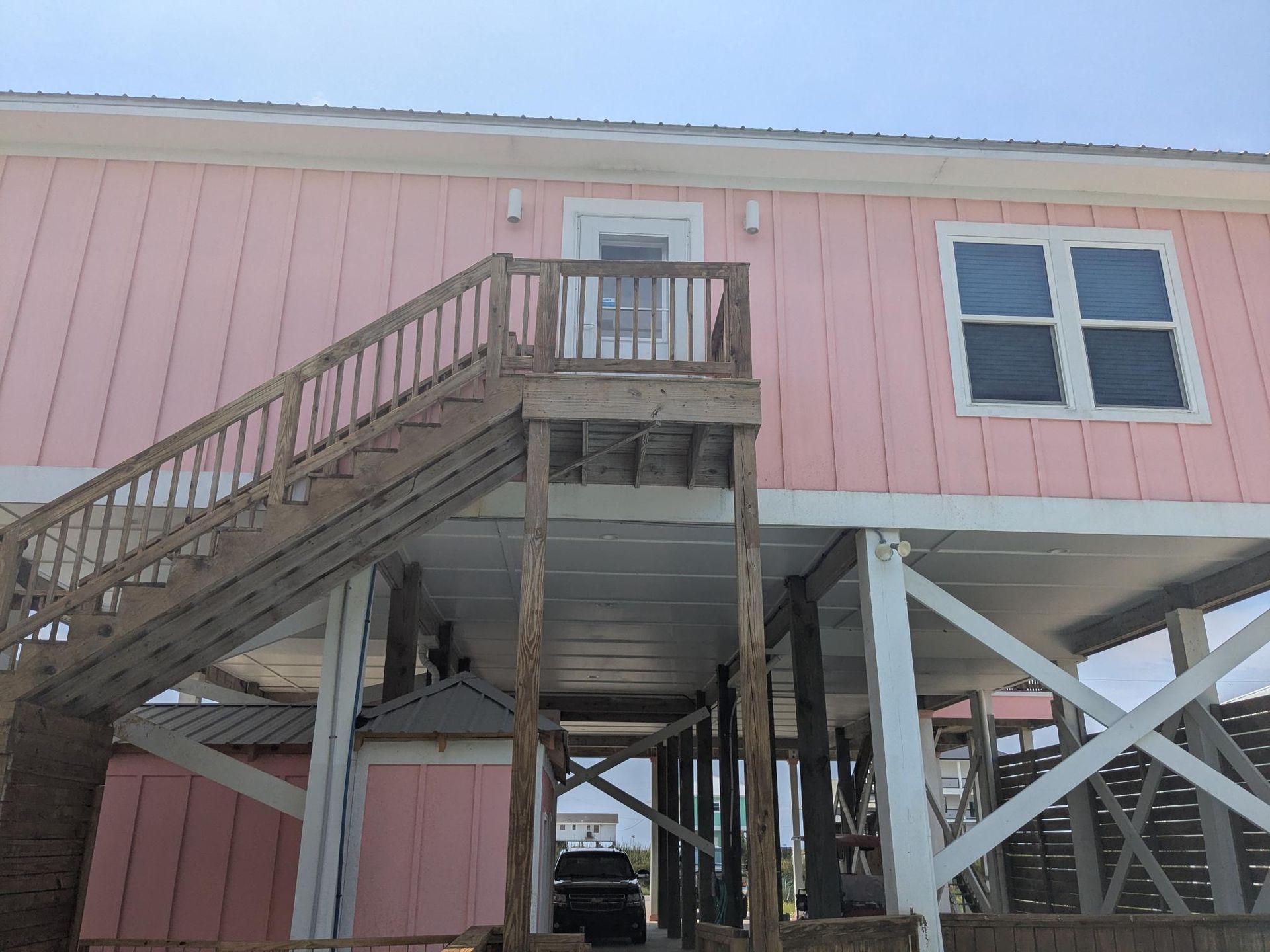 Pink beach house on stilts with wooden staircase leading to a door.