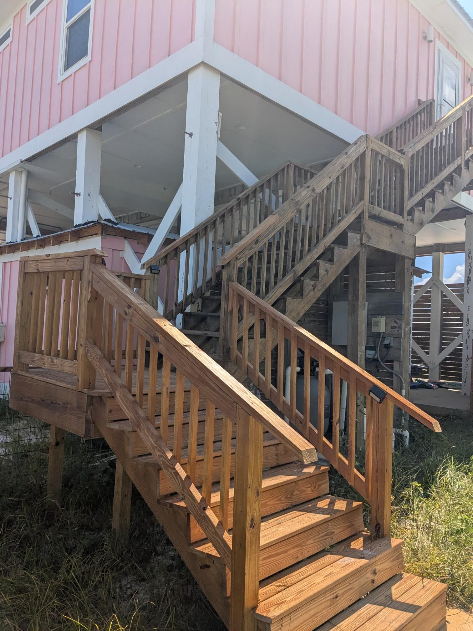 Wooden staircase leading to a pink house on stilts; outdoors.