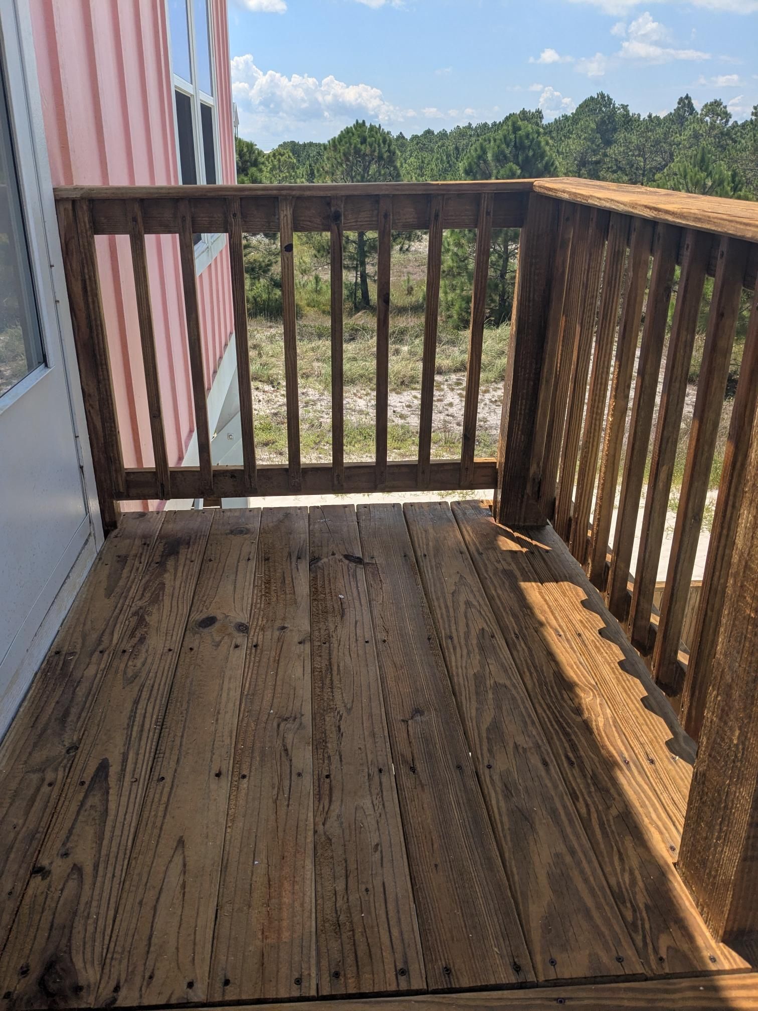 Wooden deck with railings overlooking a sandy, wooded area.