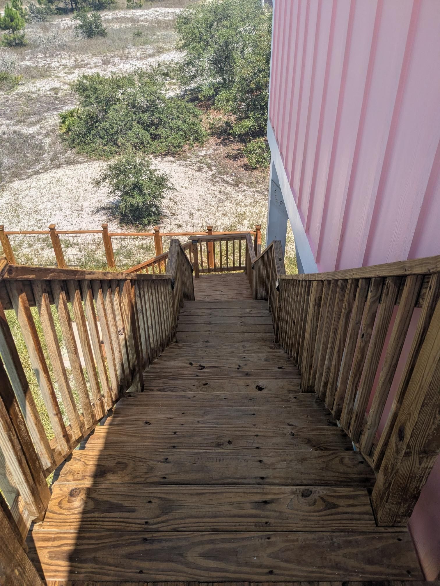 Wooden staircase descending from a pink building. Exterior setting, natural light.