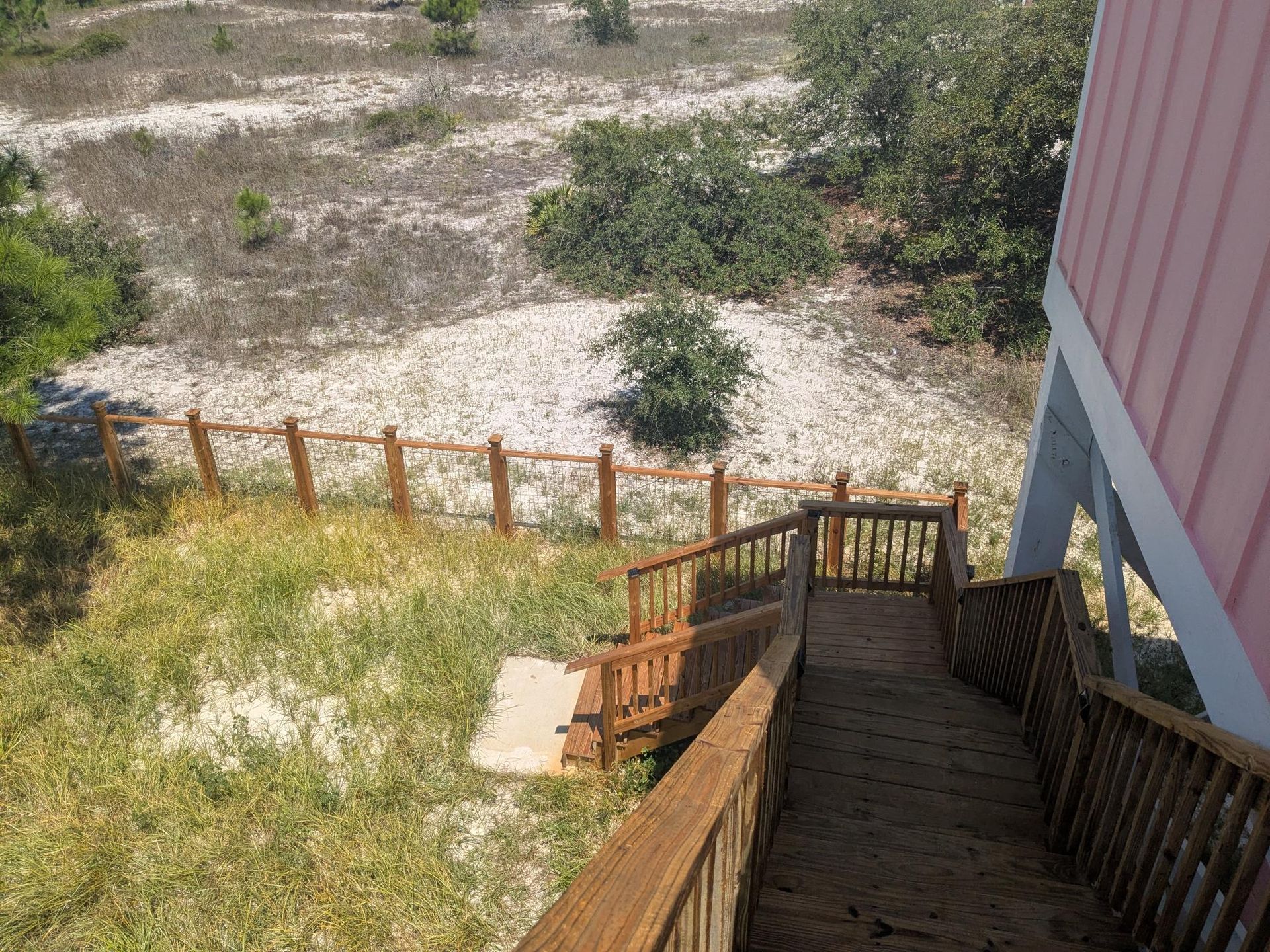 Wooden staircase leading down to sandy yard with a small fence, and a partially visible pink house.