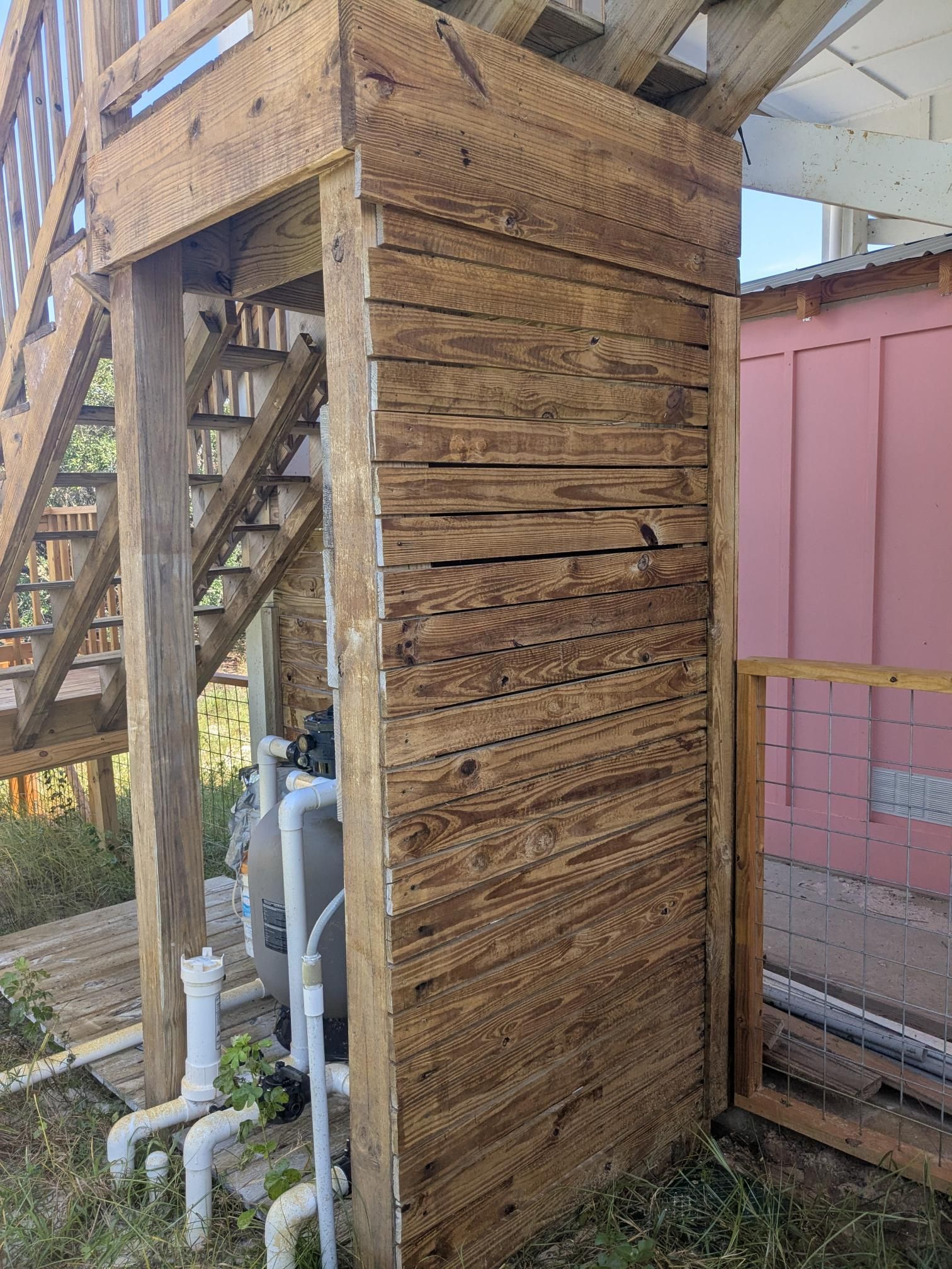 Wooden structure supporting stairs, near a pool filter, and pink building.