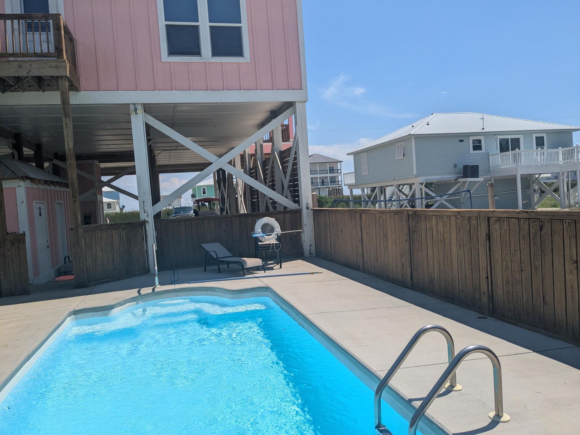 A pink house with a pool in front, next to a wooden fence. Clear sky.