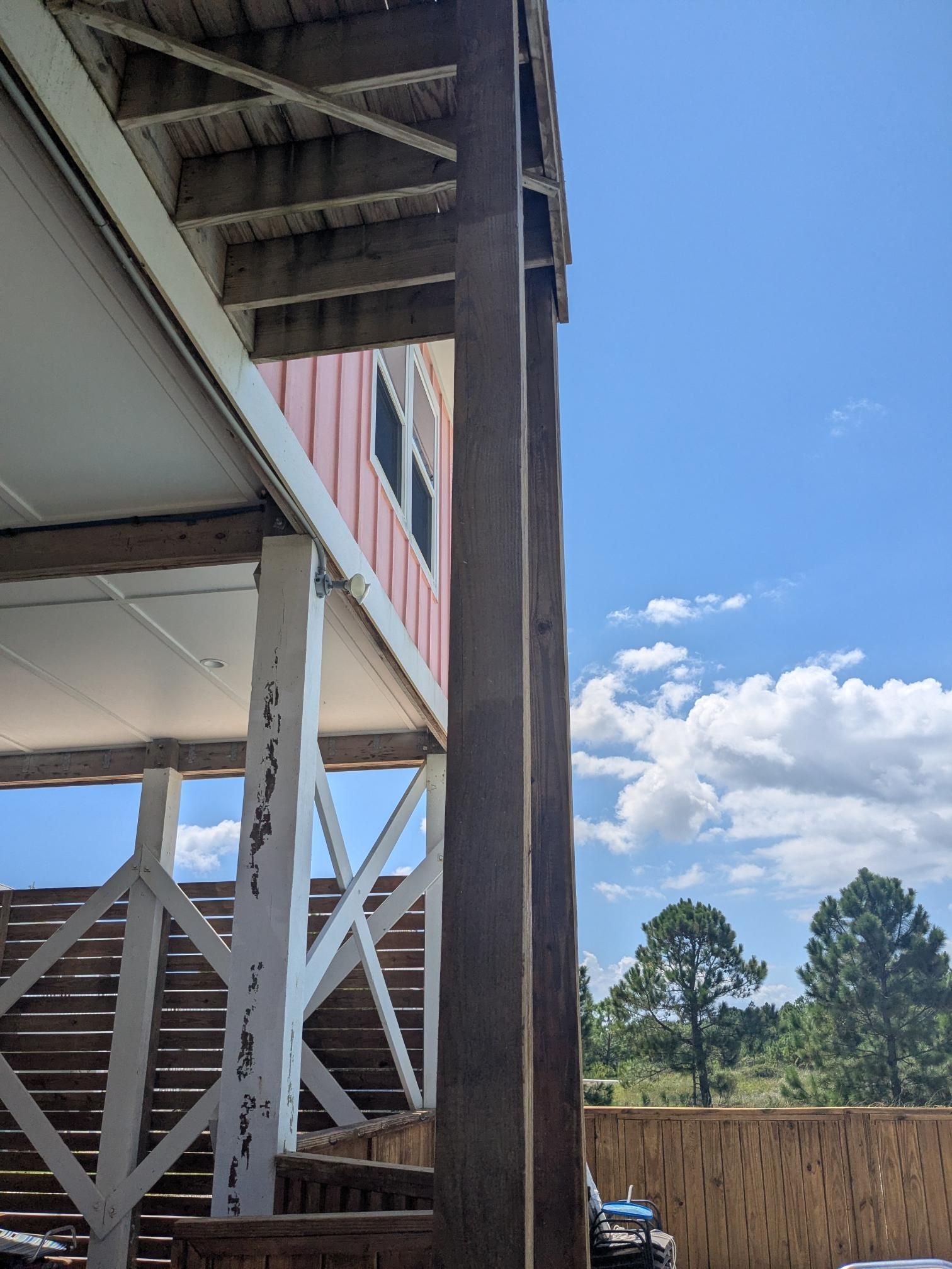 View of a building's exterior with a wooden post, stairs, and blue sky with clouds.