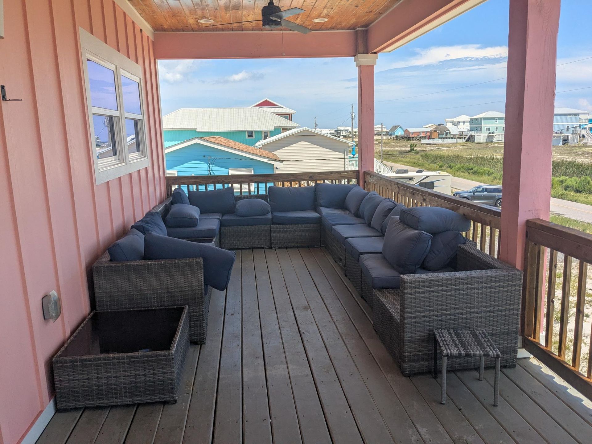 Covered porch with gray wicker sectional seating, view of beach houses and road.