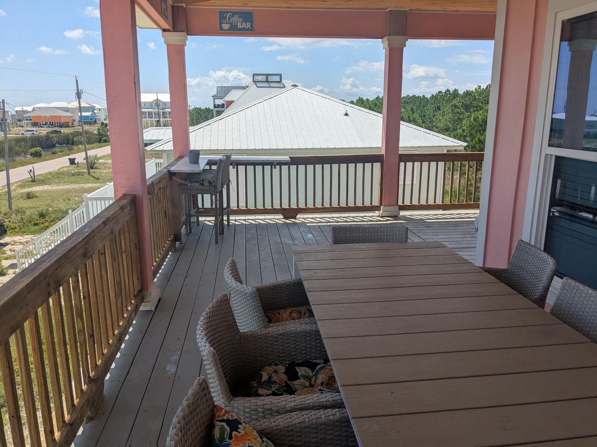 Deck with a table and chairs, overlooking a neighborhood with houses and blue sky.