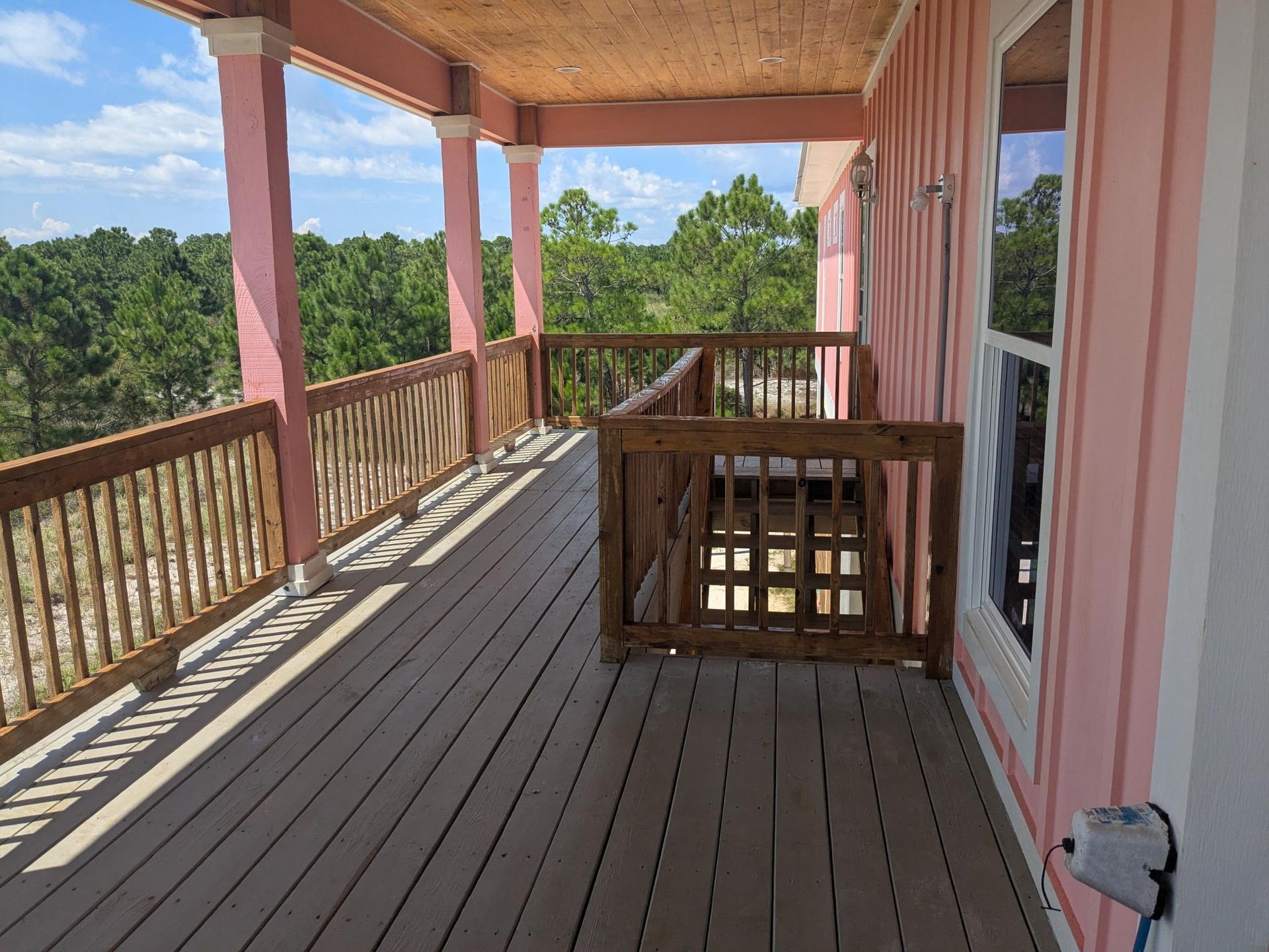 Pink porch with wooden railing, overlooking a forest. Sunlight casts shadows.