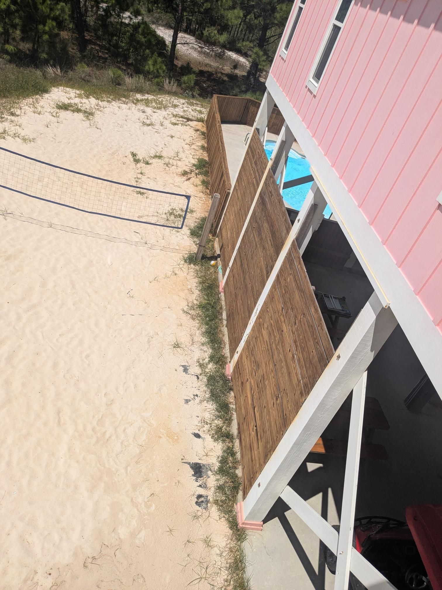 Pink beach house with woven wood paneling, volleyball net on sandy ground.