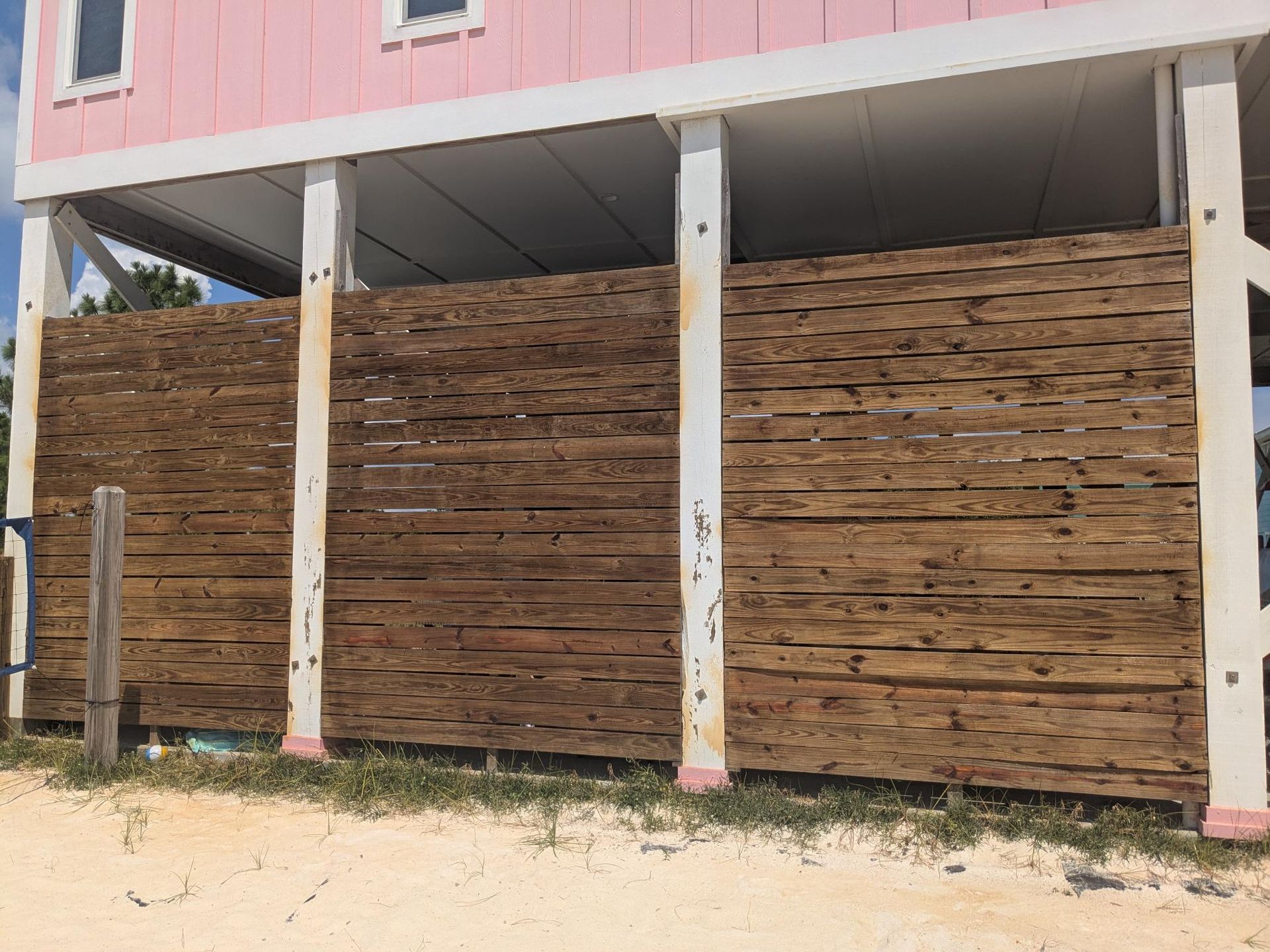 Pink beach house with wooden lattice skirting, supported by white pillars.