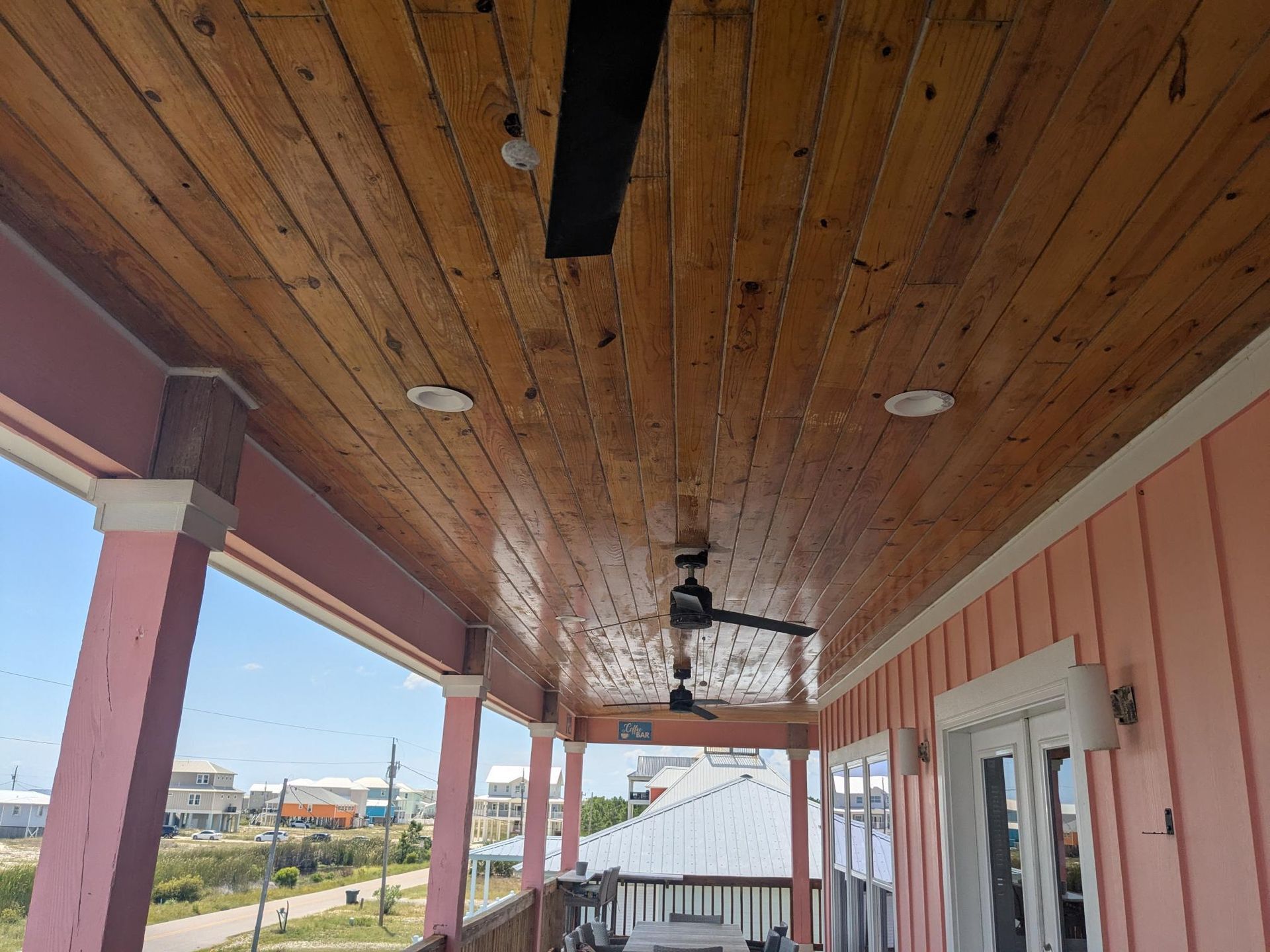 Porch ceiling with wood planks, ceiling fans, and recessed lights; pink trim and exterior walls.