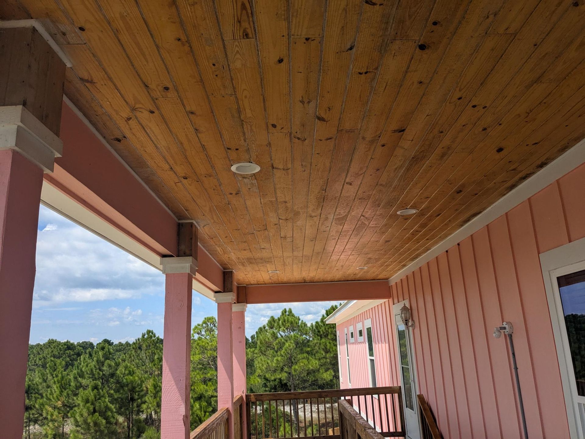 Pink porch with wooden ceiling, columns, and view of trees and sky.