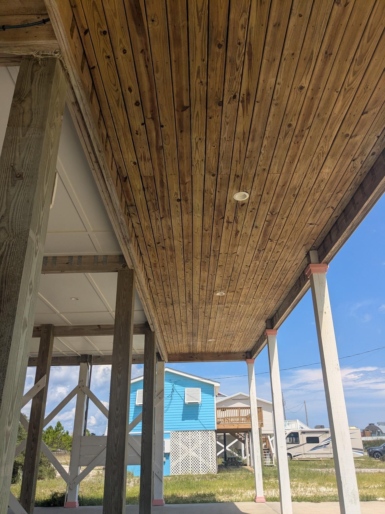 Wooden ceiling of a porch, supported by concrete and wood posts, overlooking a coastal scene.