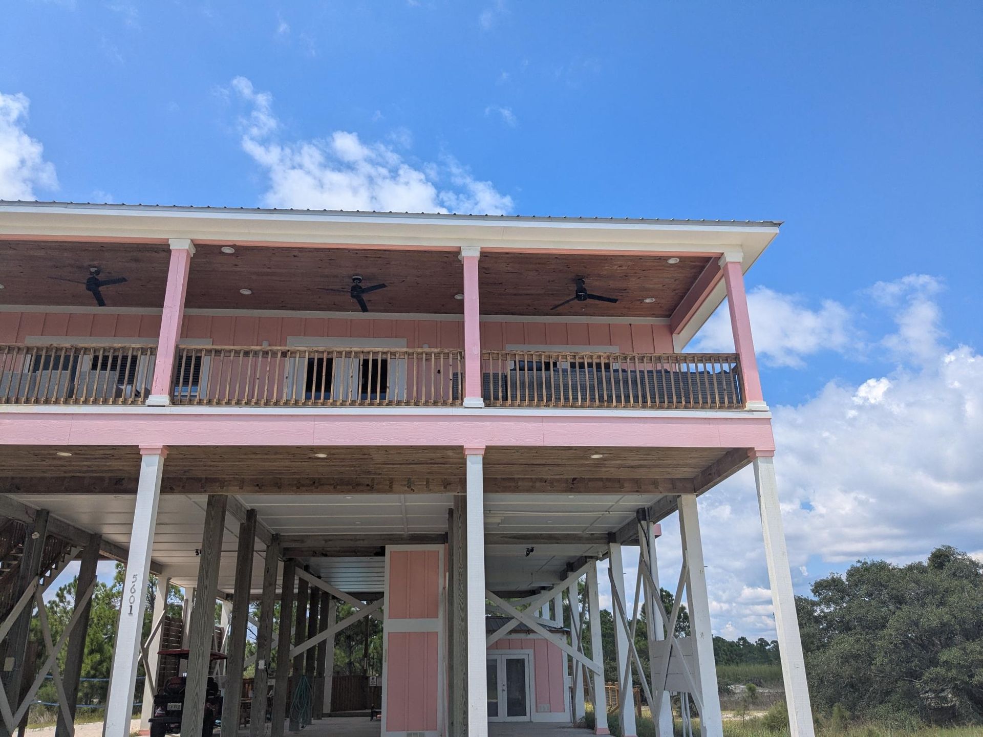 Pink beach house on stilts with a balcony, under a blue sky with clouds.