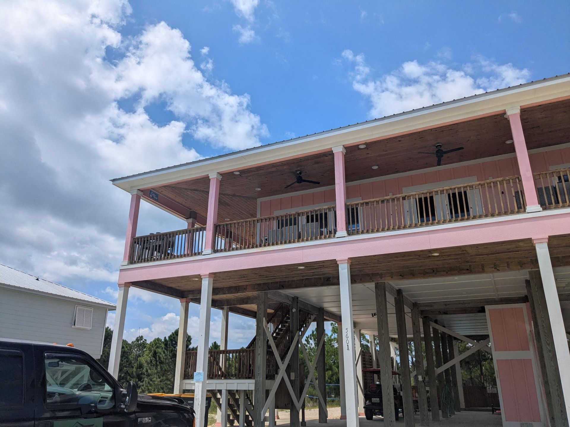 Pink beach house on stilts with wooden balconies, set against a blue sky with clouds.
