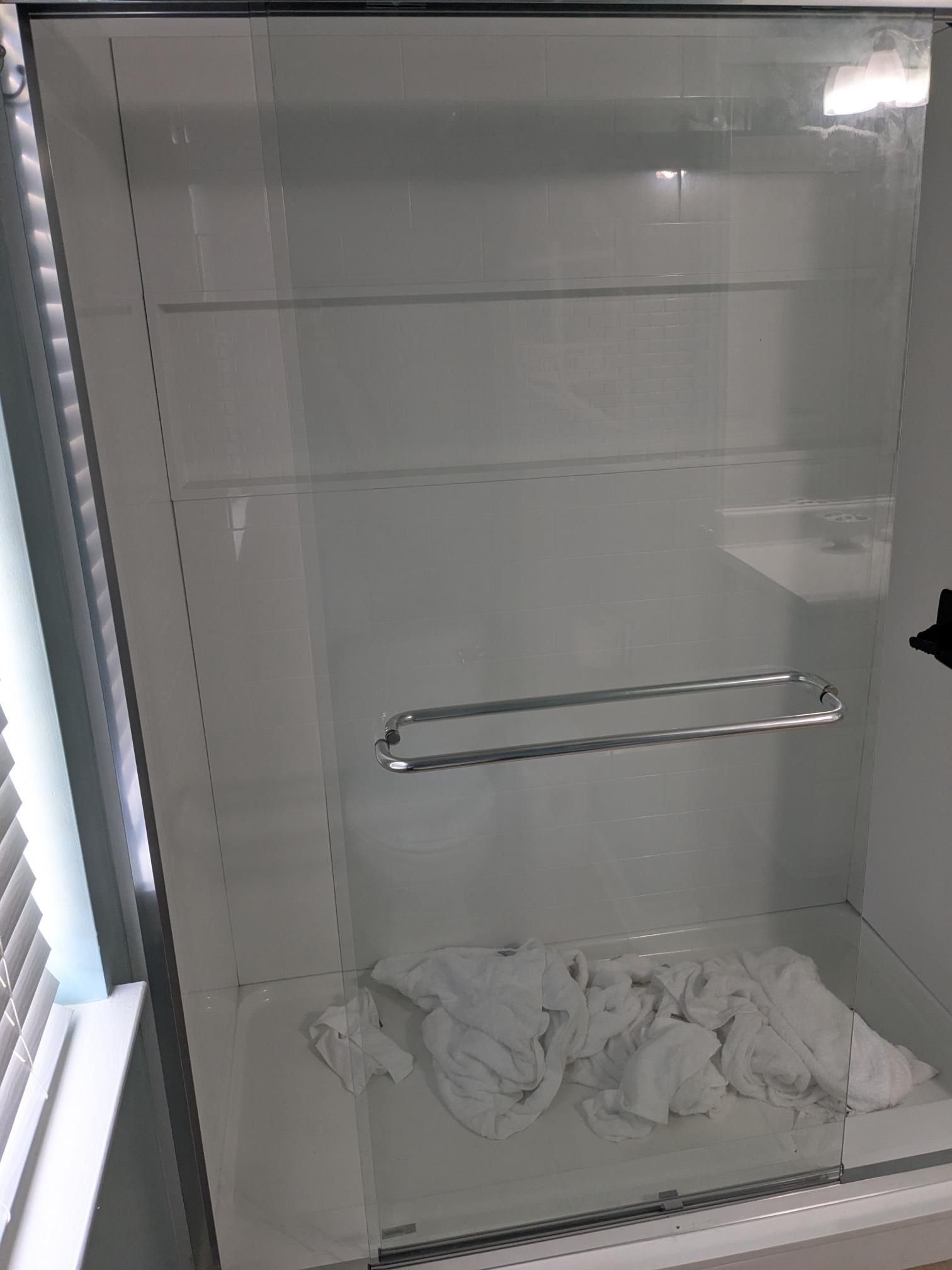 Empty glass shower with a towel rack and white towels on the floor.