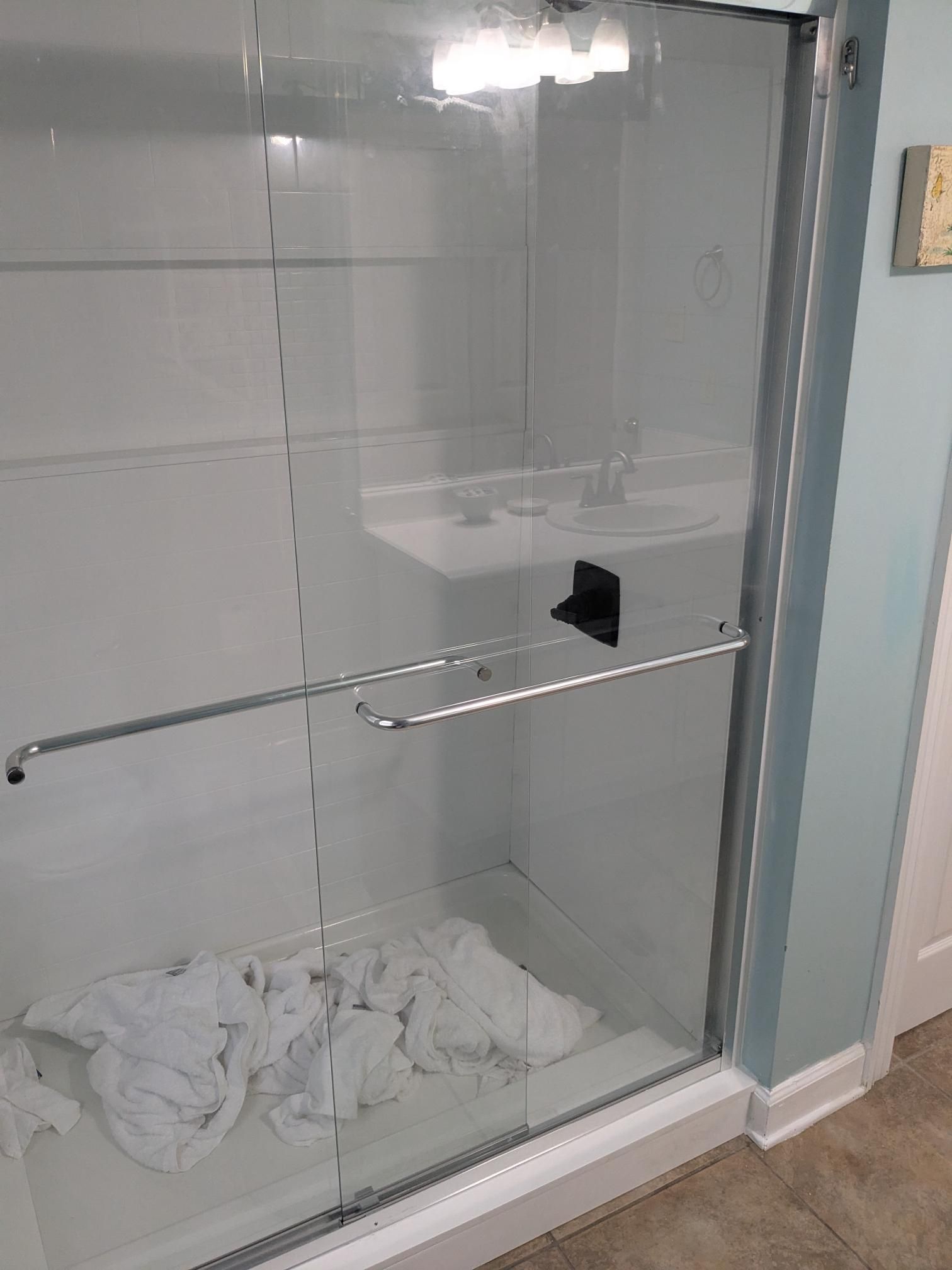 A glass shower with a white interior and a pile of white laundry on the floor.