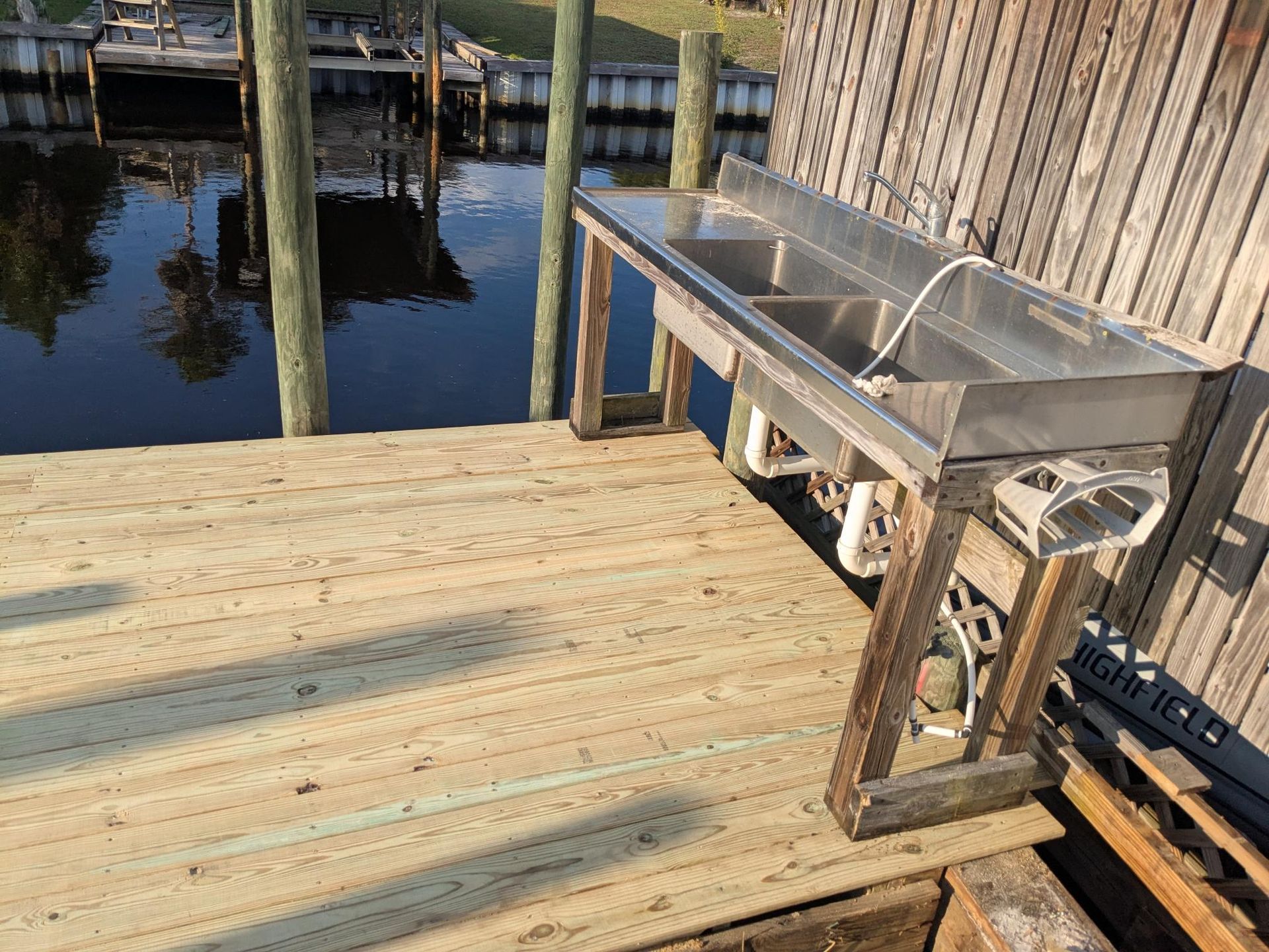 A stainless steel fish cleaning station on a wooden dock next to a waterway.